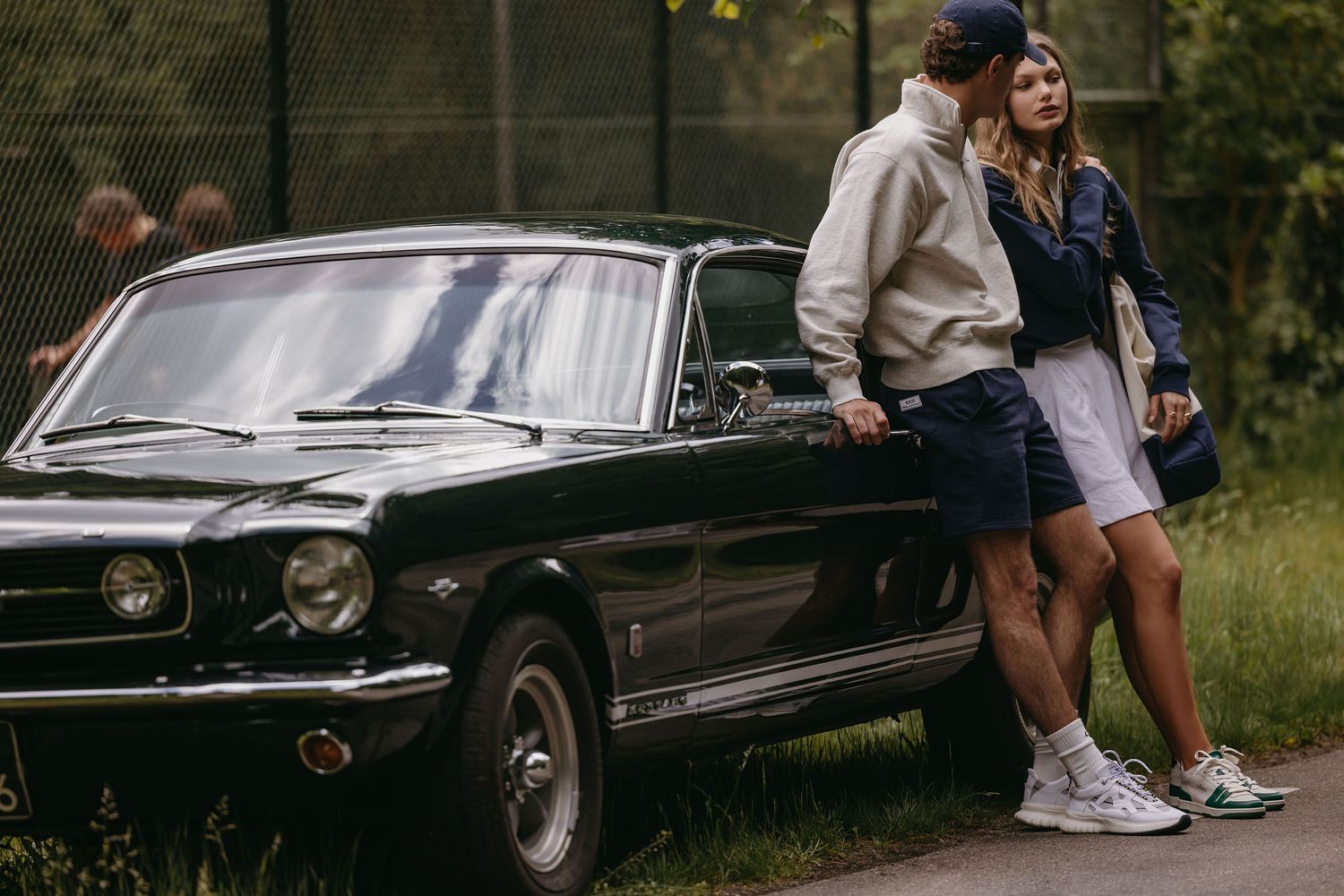 Couple posing against classic Mustang car in casual attire.