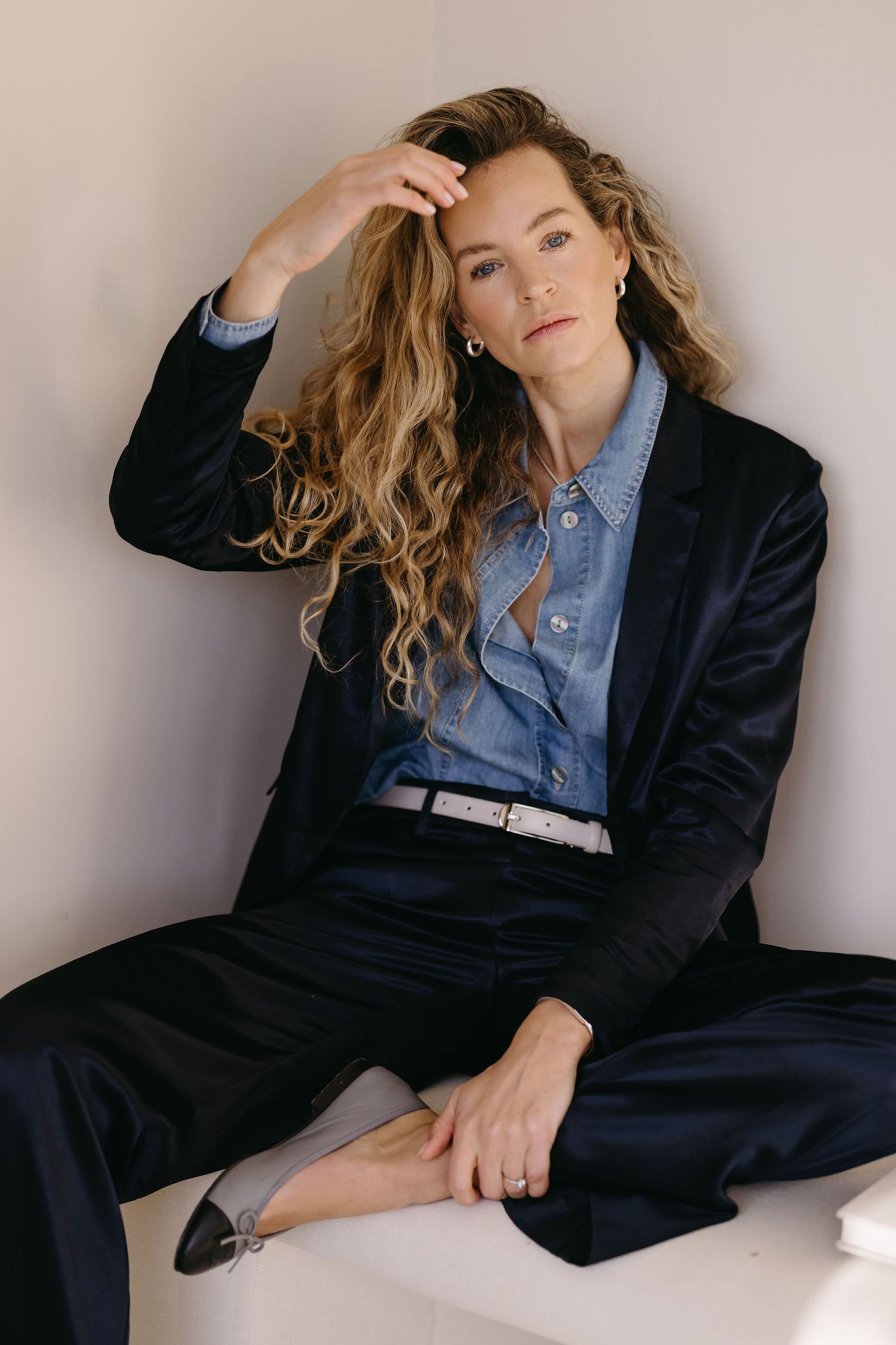 Fashion portrait featuring denim shirt and navy blazer in minimalist setting.