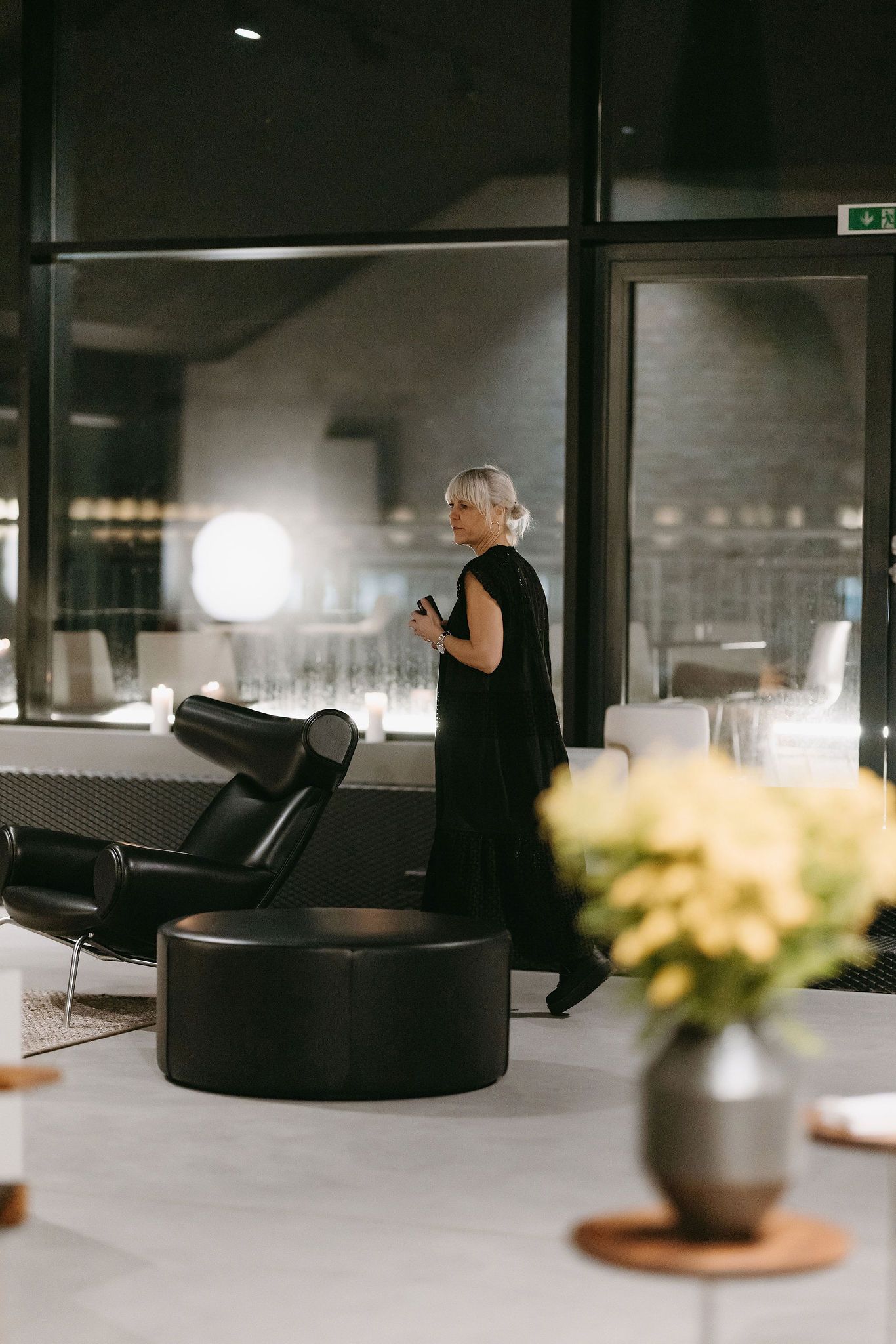 A presenter in black attire speaks in a modern conference space with stylish furniture and decor.