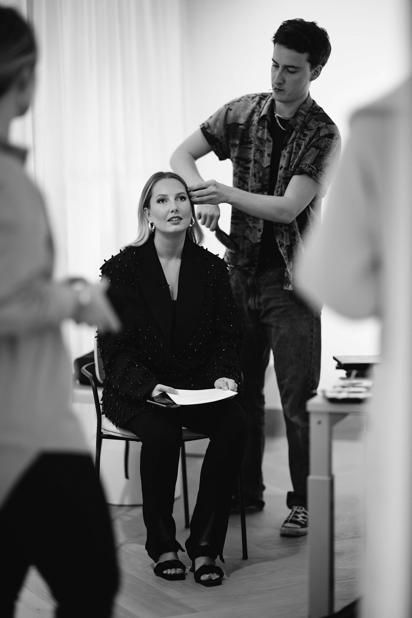 A stylist works on arranging hair in a black and white behind-the-scenes photo shoot setting.