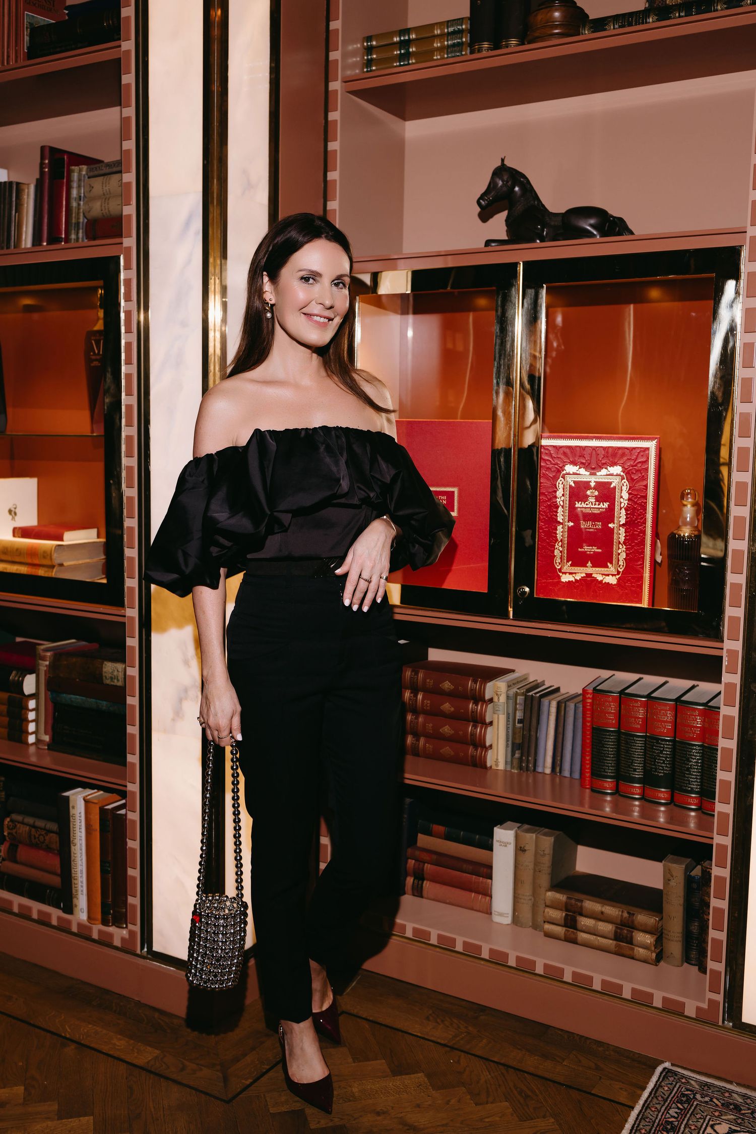 An elegant evening look featuring a black off-shoulder ruffle dress in a luxurious library setting.