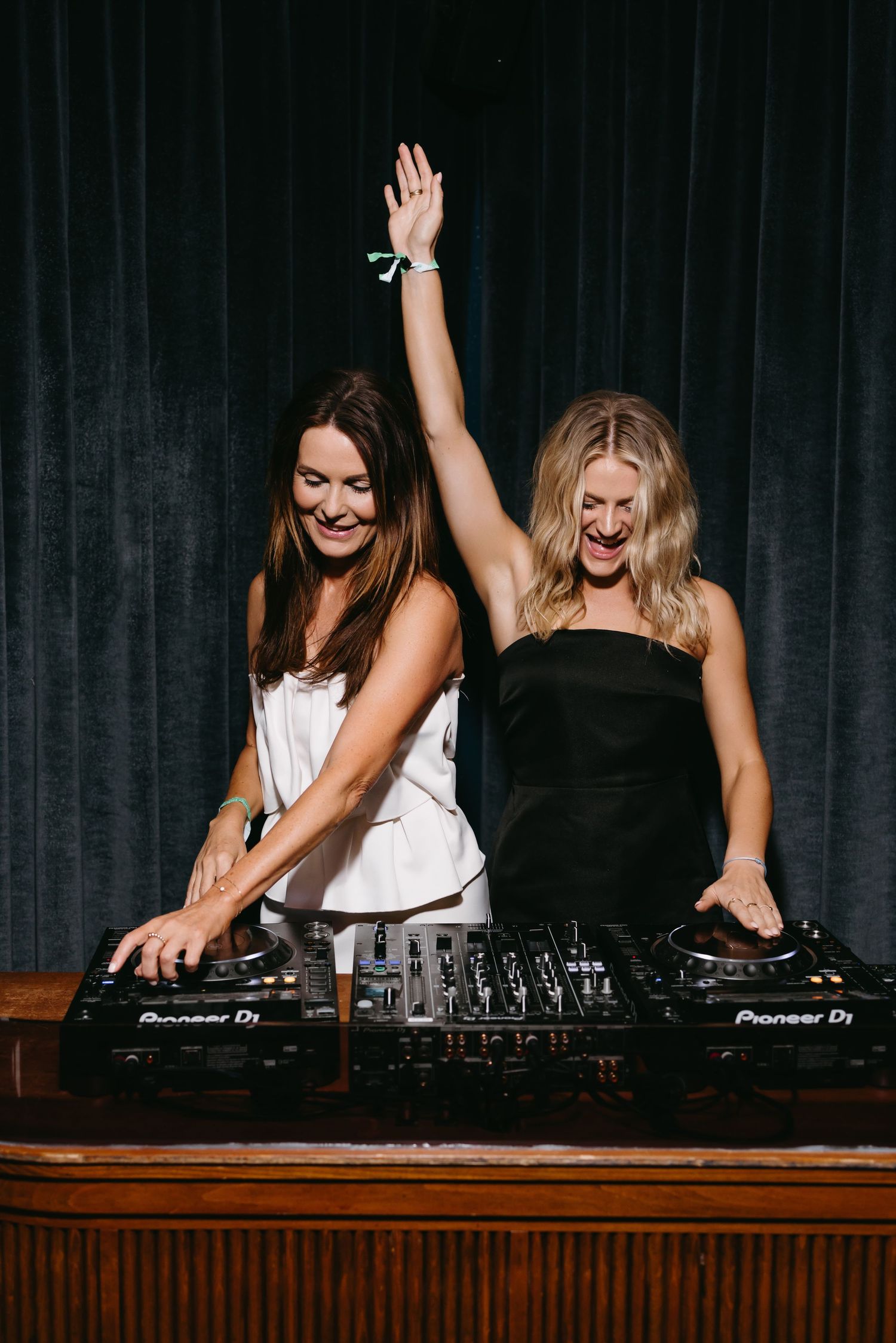 Two DJs performing enthusiastically at Pioneer DJ equipment with black curtain backdrop.