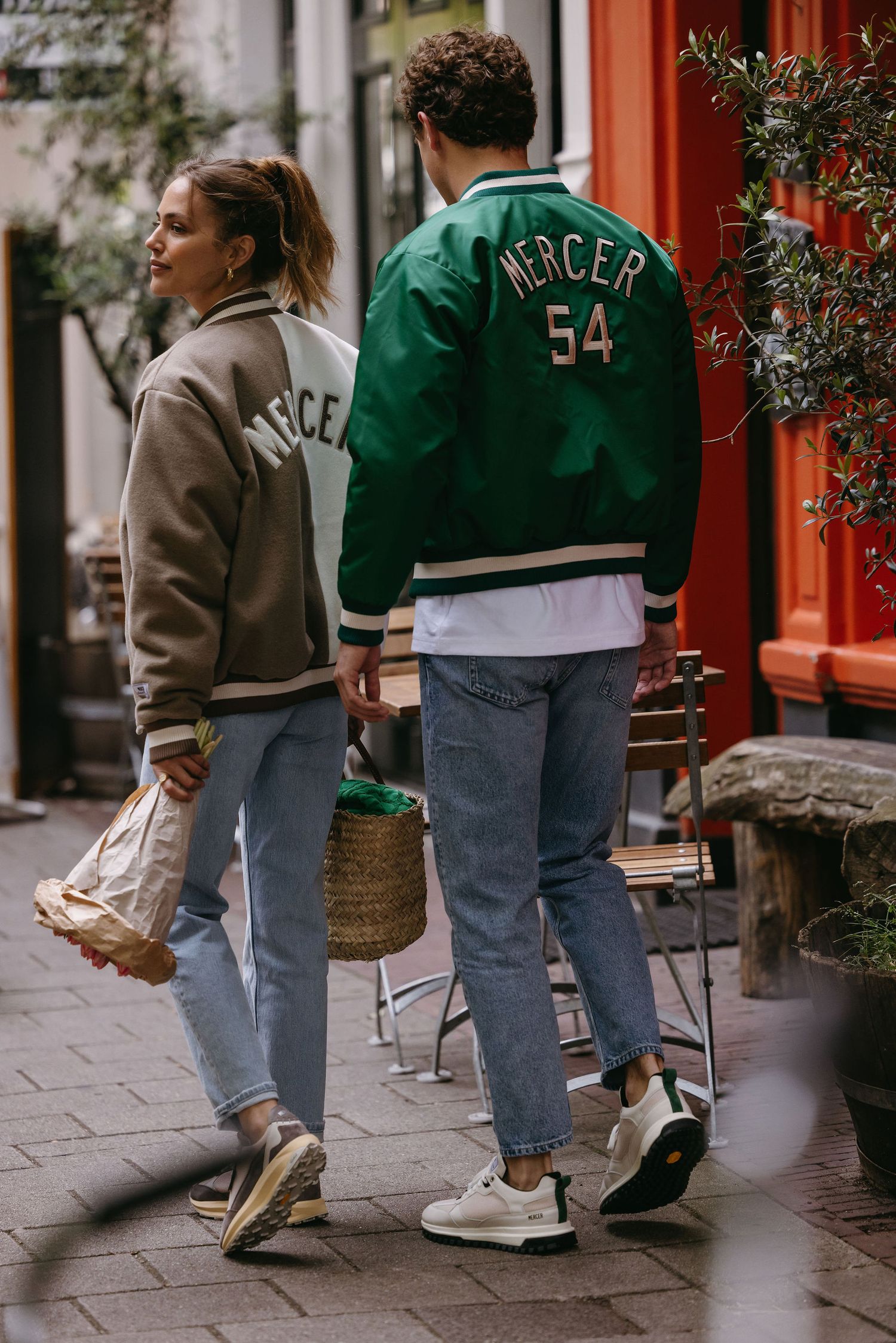 Couple wearing matching varsity jackets walking on cobblestone street.