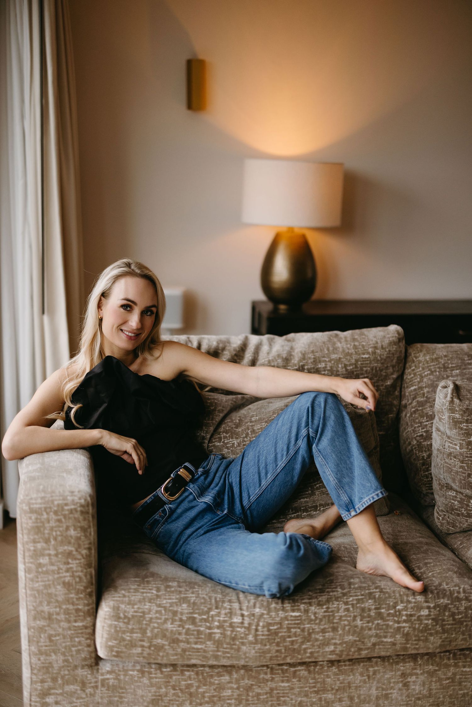 Relaxed casual style with jeans and black top while lounging on grey sofa.