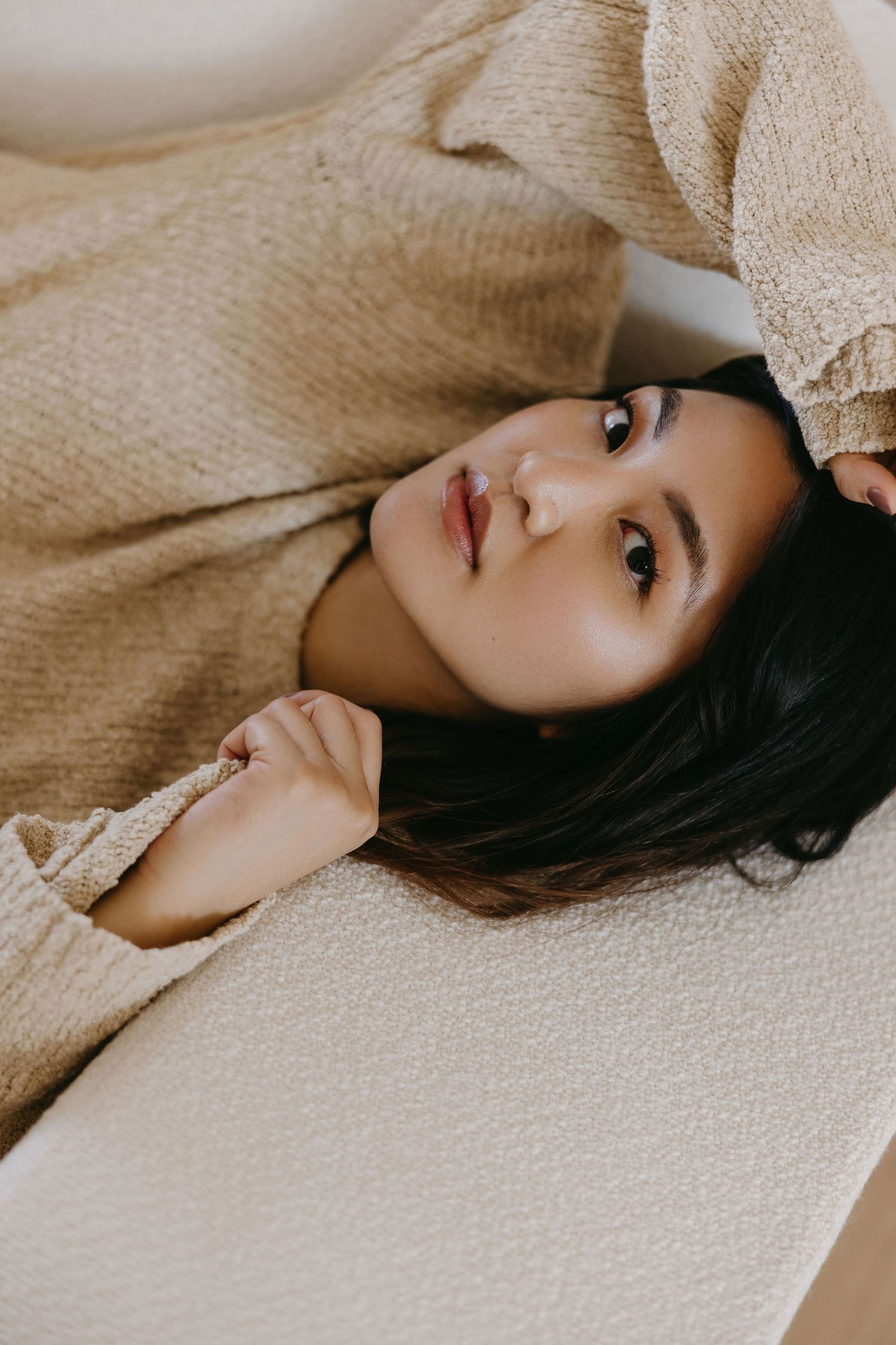 Portrait of someone lying down in a beige sweater with soft lighting and dreamy expression.