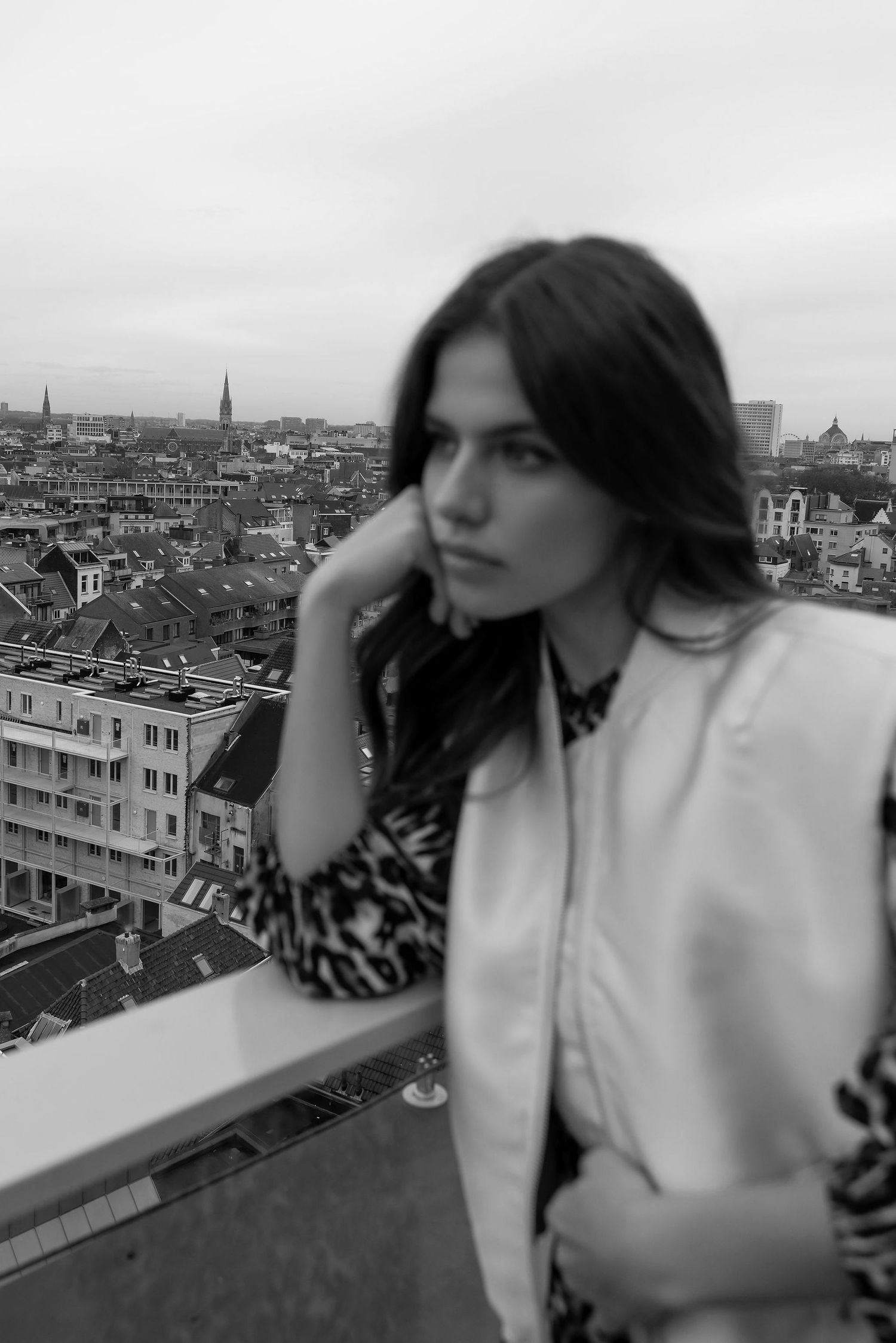 Moody cityscape portrait featuring leopard print and white blazer overlooking European rooftops.