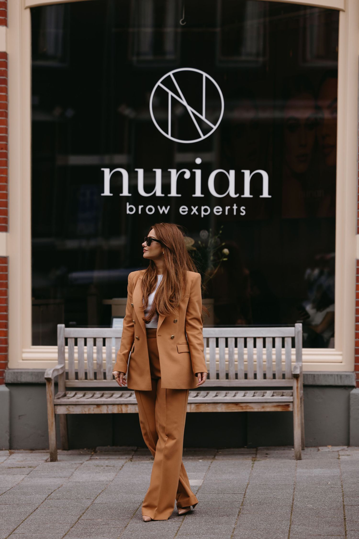 Stylish tan pantsuit outfit in front of Nurian brow experts storefront with wooden bench.