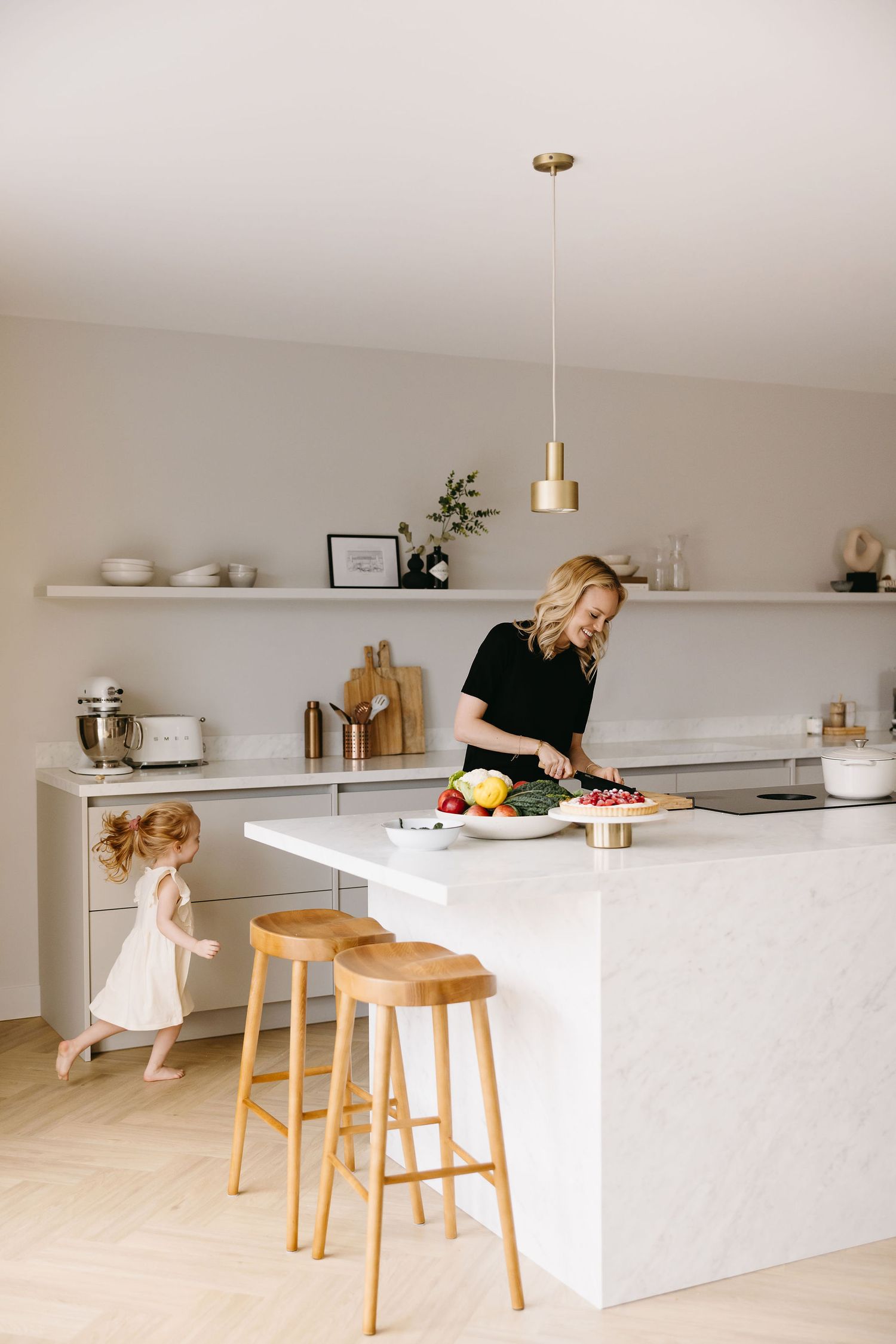 Bright kitchen interior with white countertops and wooden stools while someone prepares food.