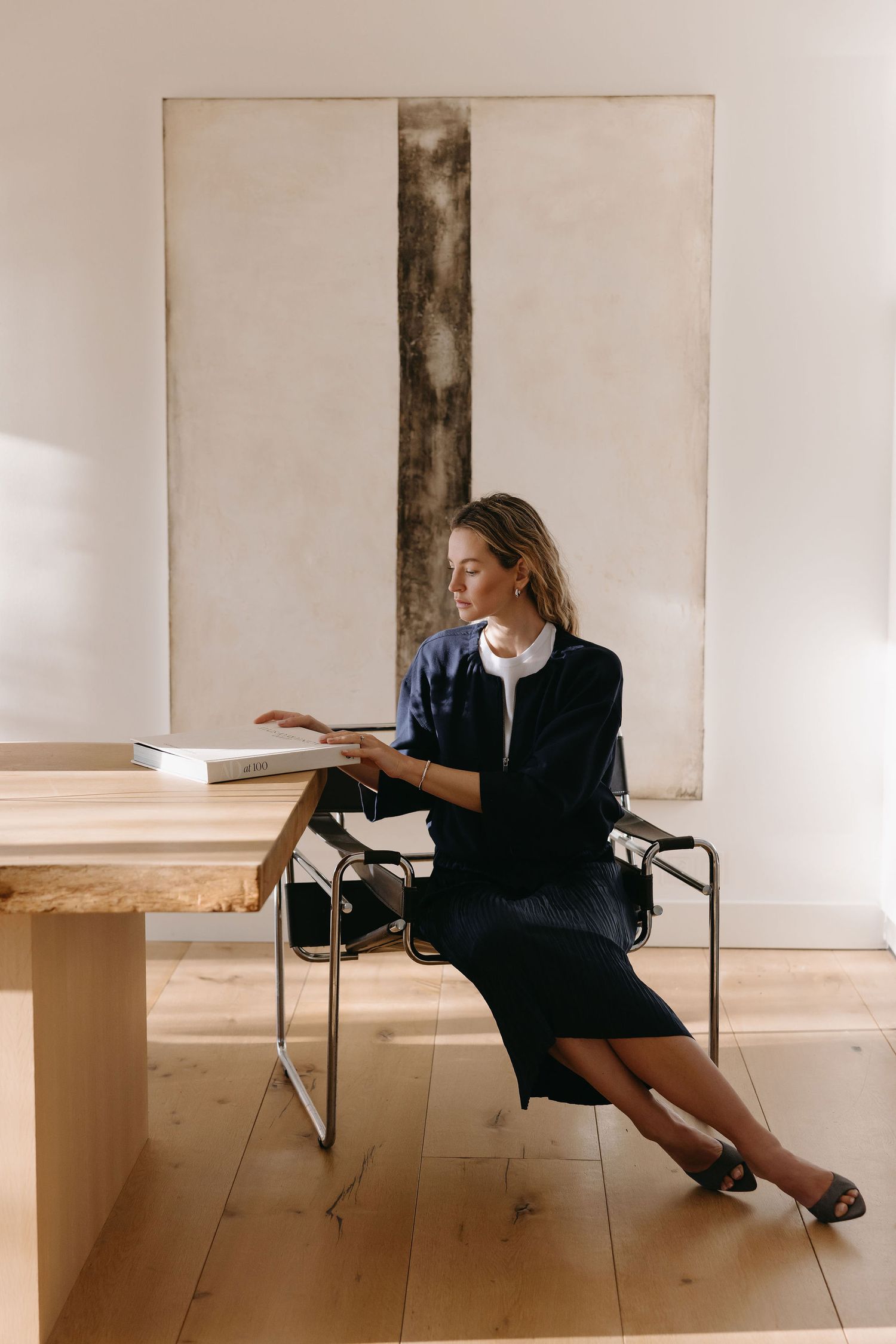Professional seated in a stylish office chair wearing a navy blue outfit against a minimalist white backdrop.