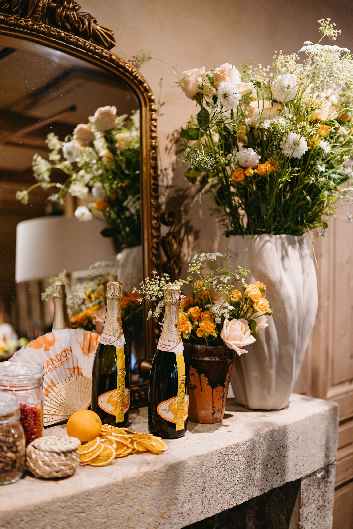 Elegant table setting with floral arrangements, champagne bottles and citrus decorations in front of ornate mirror.