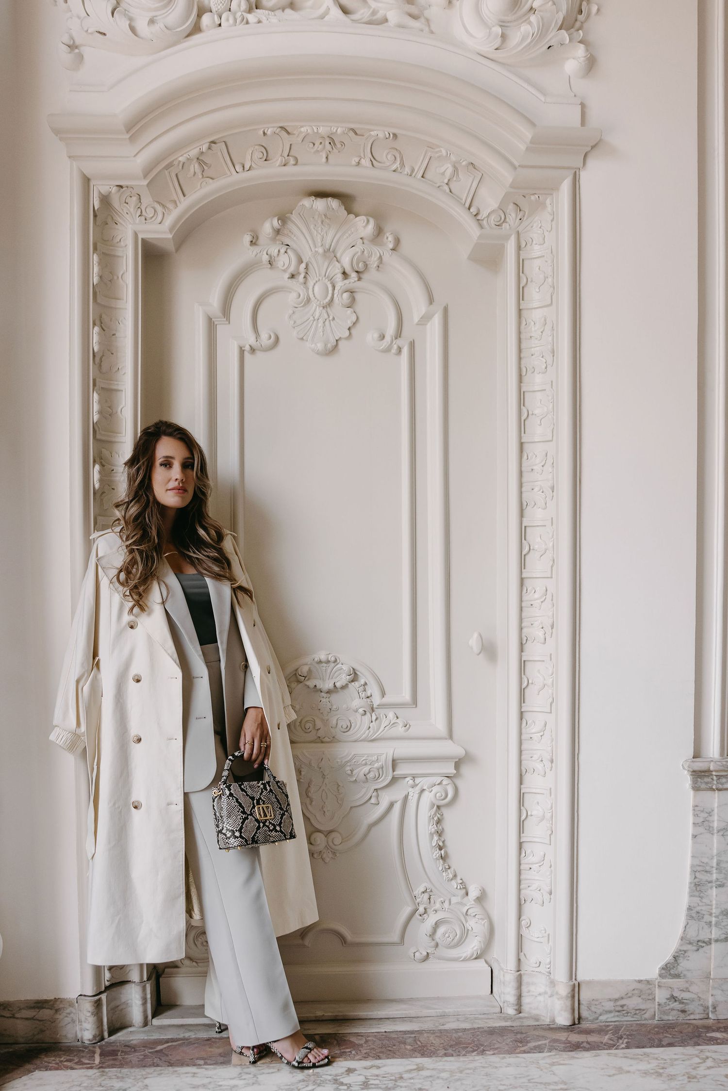 Elegant fashion pose against ornate white architectural wall with decorative moldings.