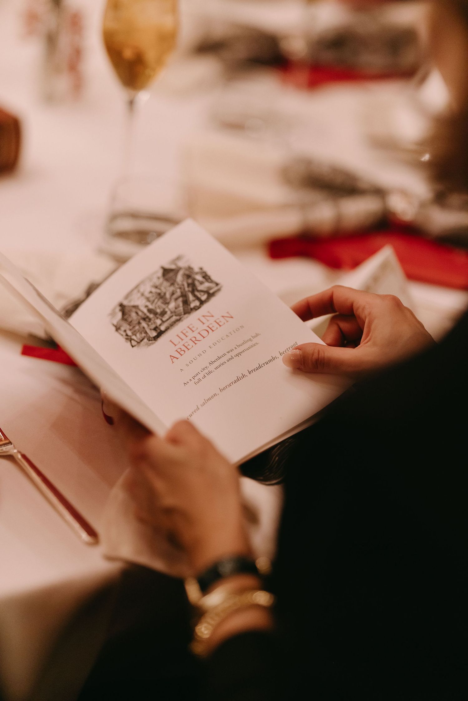 Close-up shot of hands holding an elegant menu against a white tablecloth.