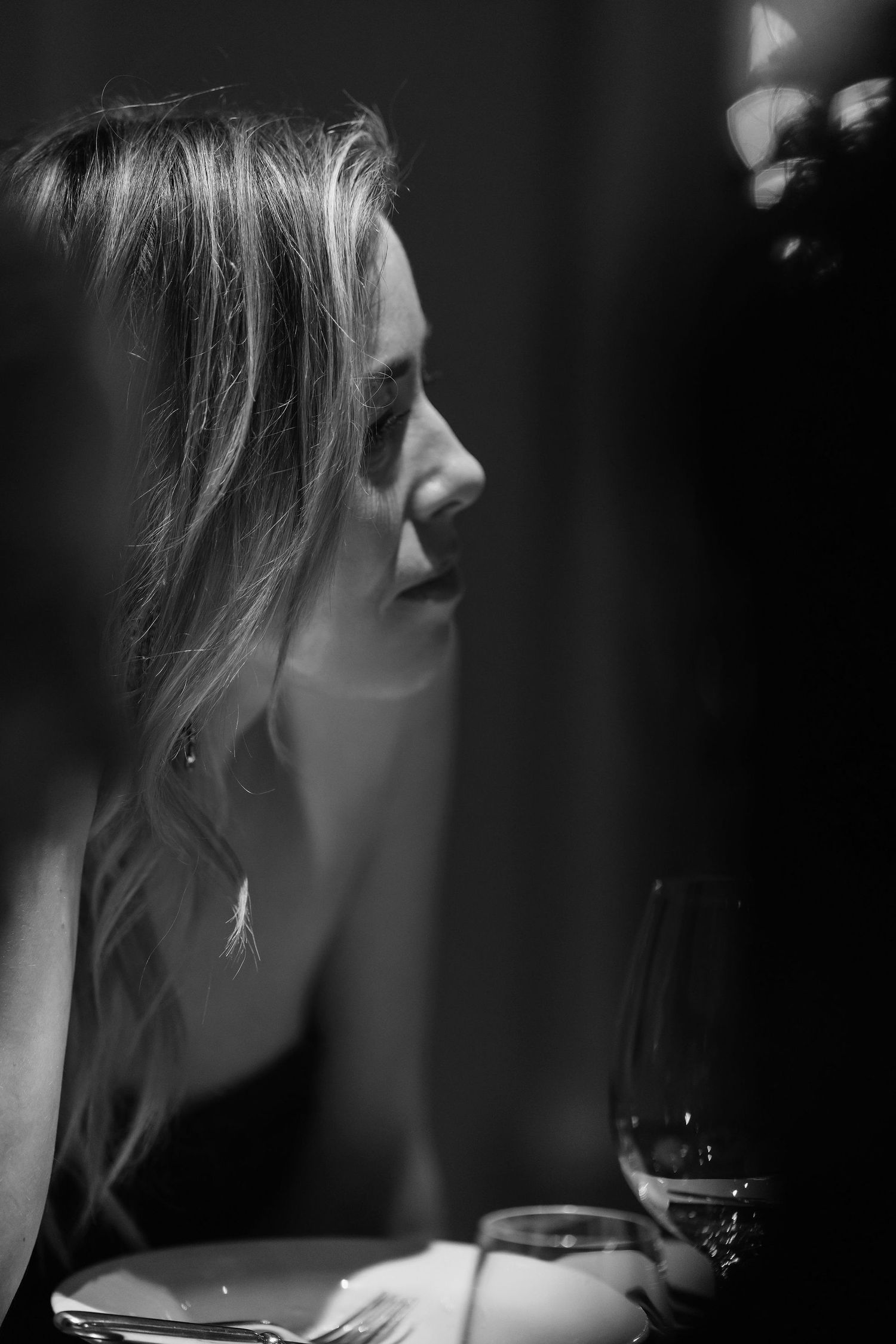 Black and white profile portrait of person with wine glass in moody lighting.