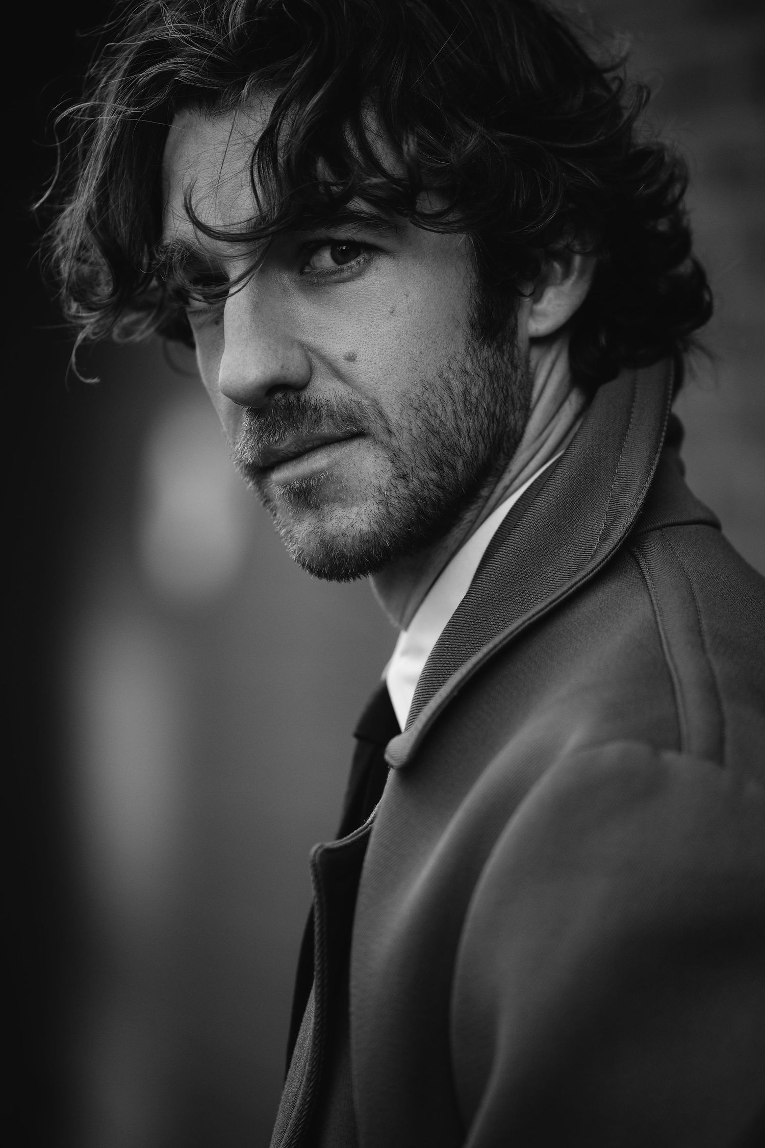 Dramatic black and white portrait of a man in formal wear with curly hair.