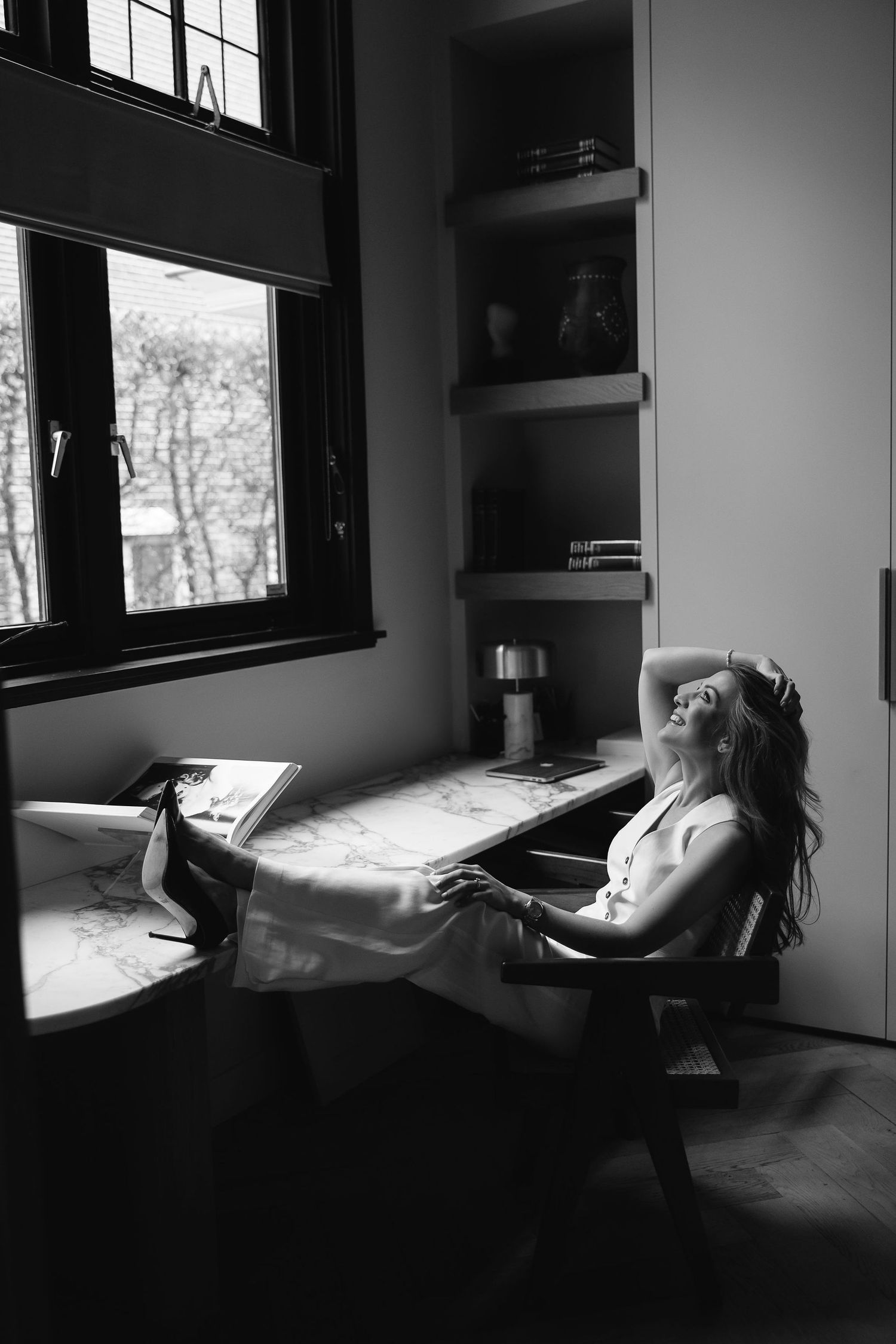 Black and white photo of person relaxing in chair by window with natural lighting.