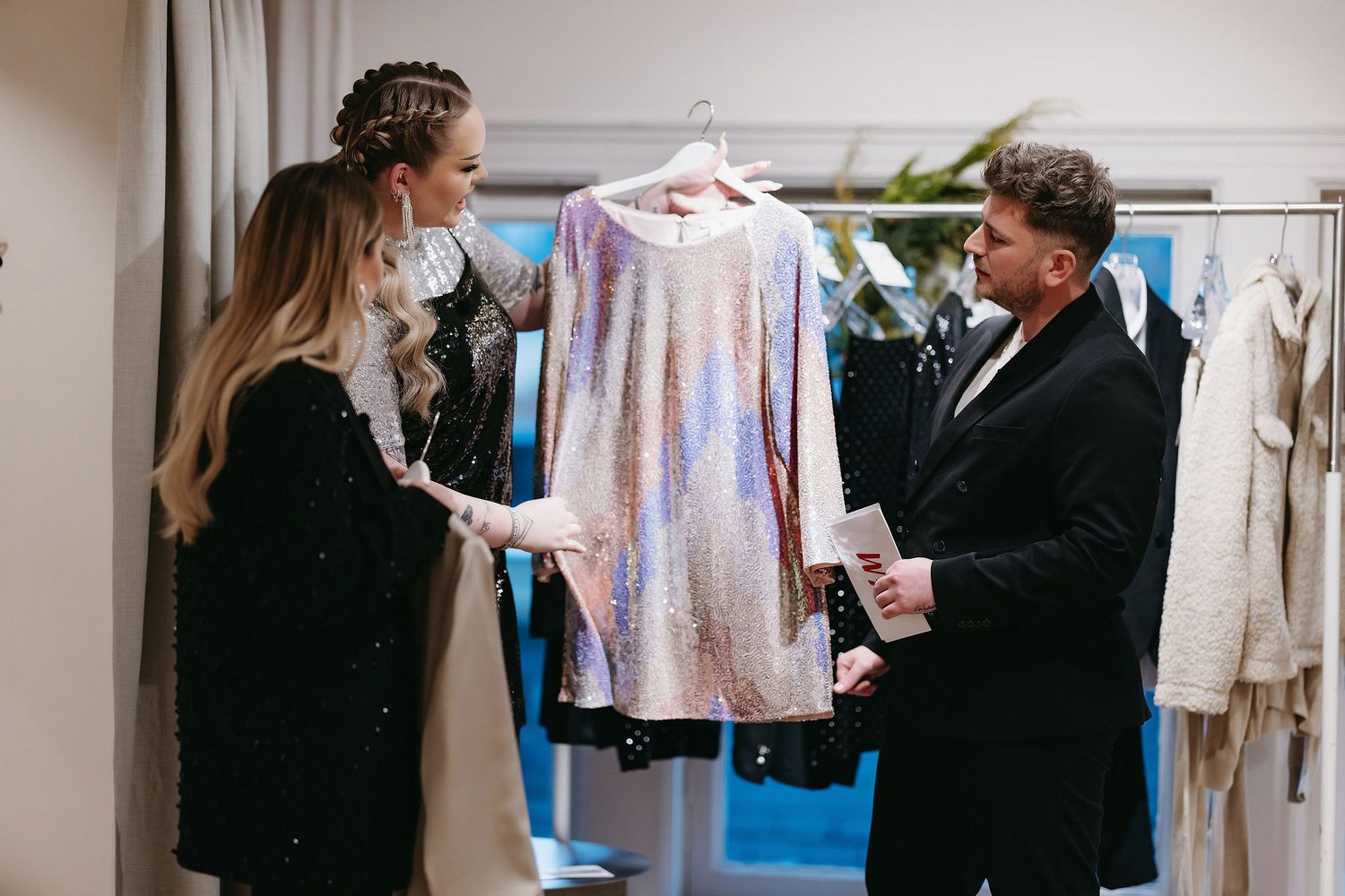 Stylists discuss a sequined dress on display in an elegant clothing boutique.