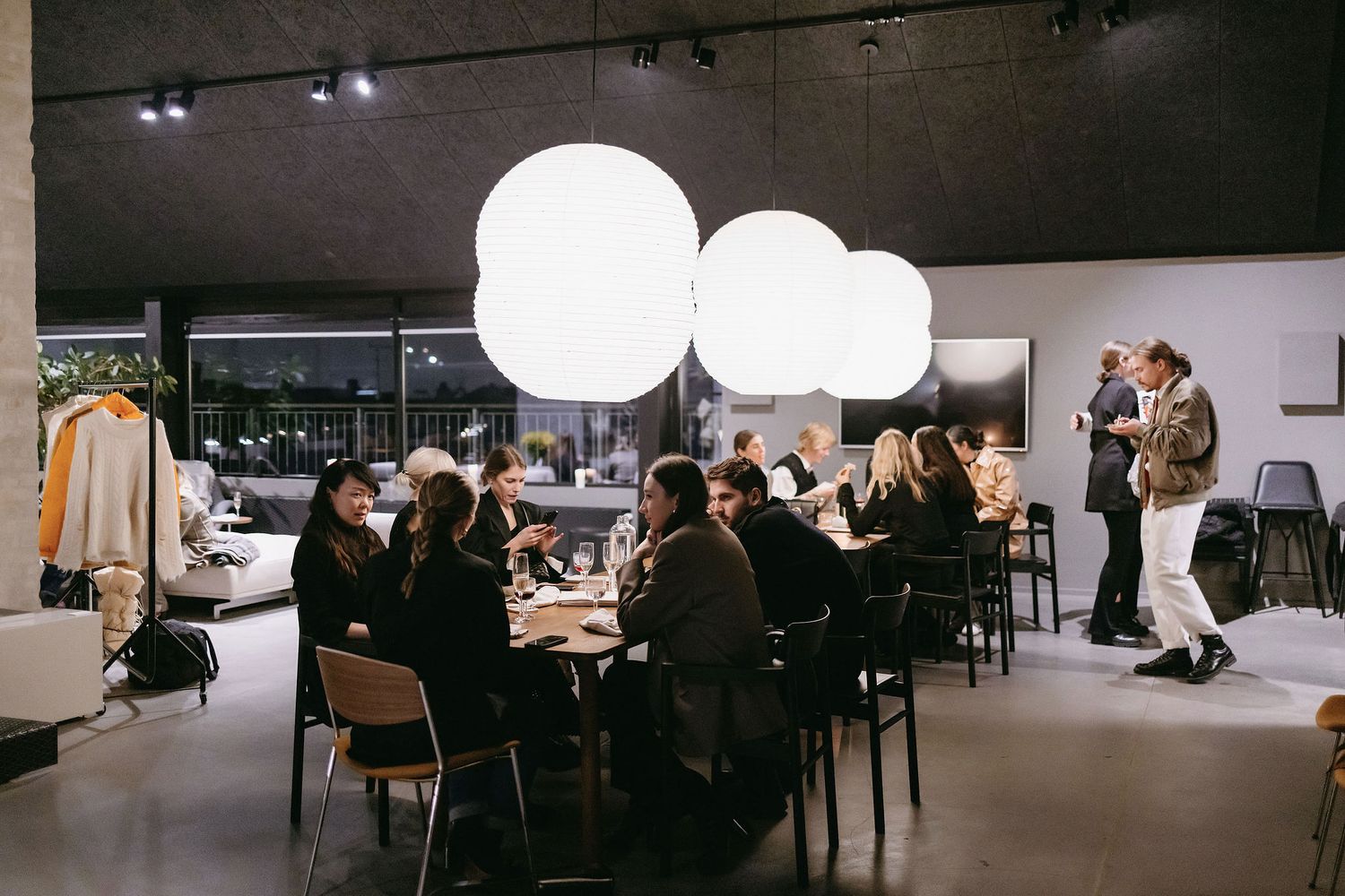 People gathered at a modern event space with large white pendant lamps and dining tables.