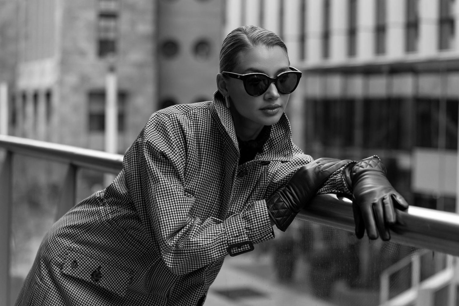 Fashion portrait in grey coat and sunglasses against urban architecture.