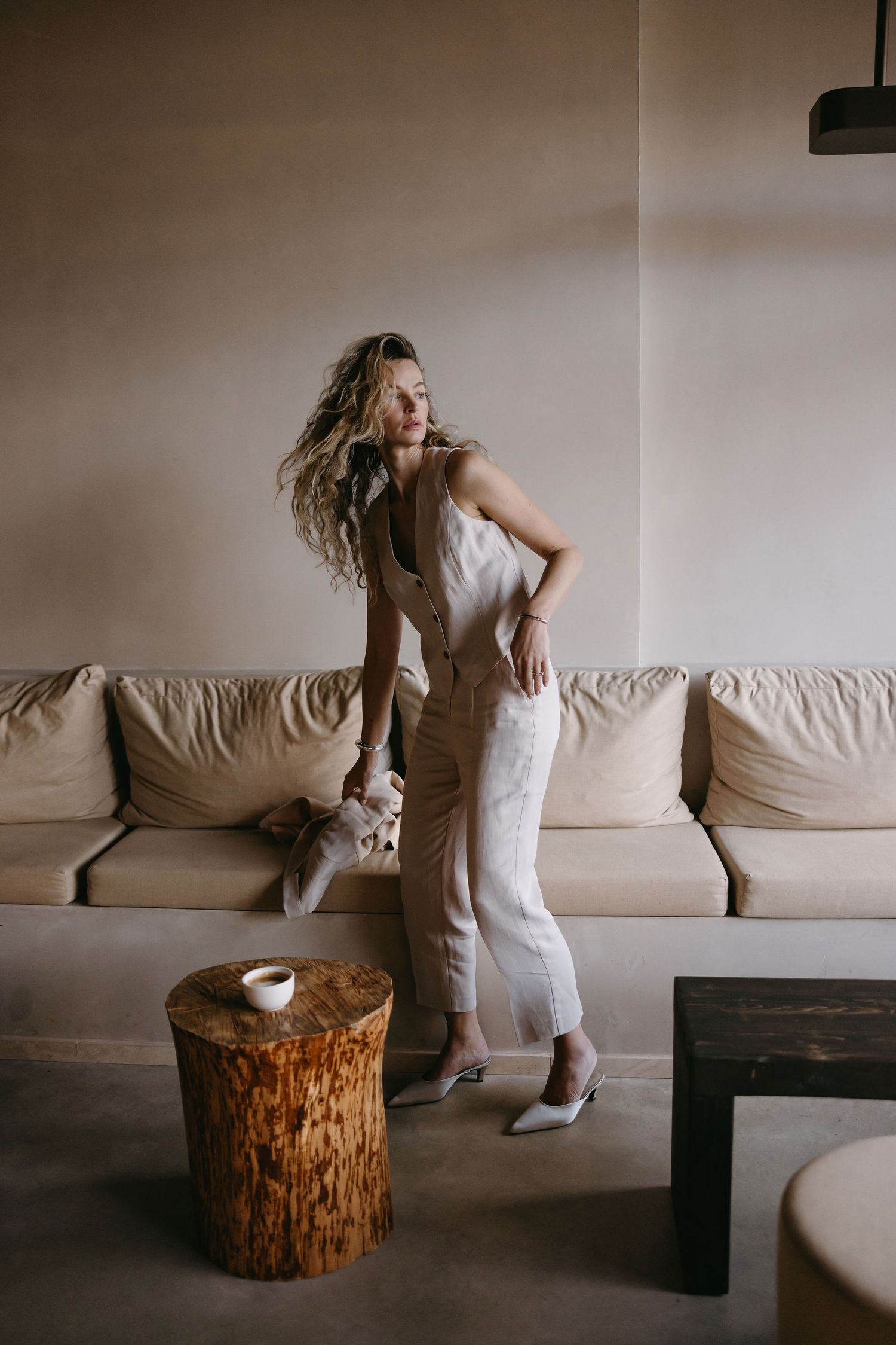 Minimalist fashion scene with beige outfit against matching sofa and wooden accent table.
