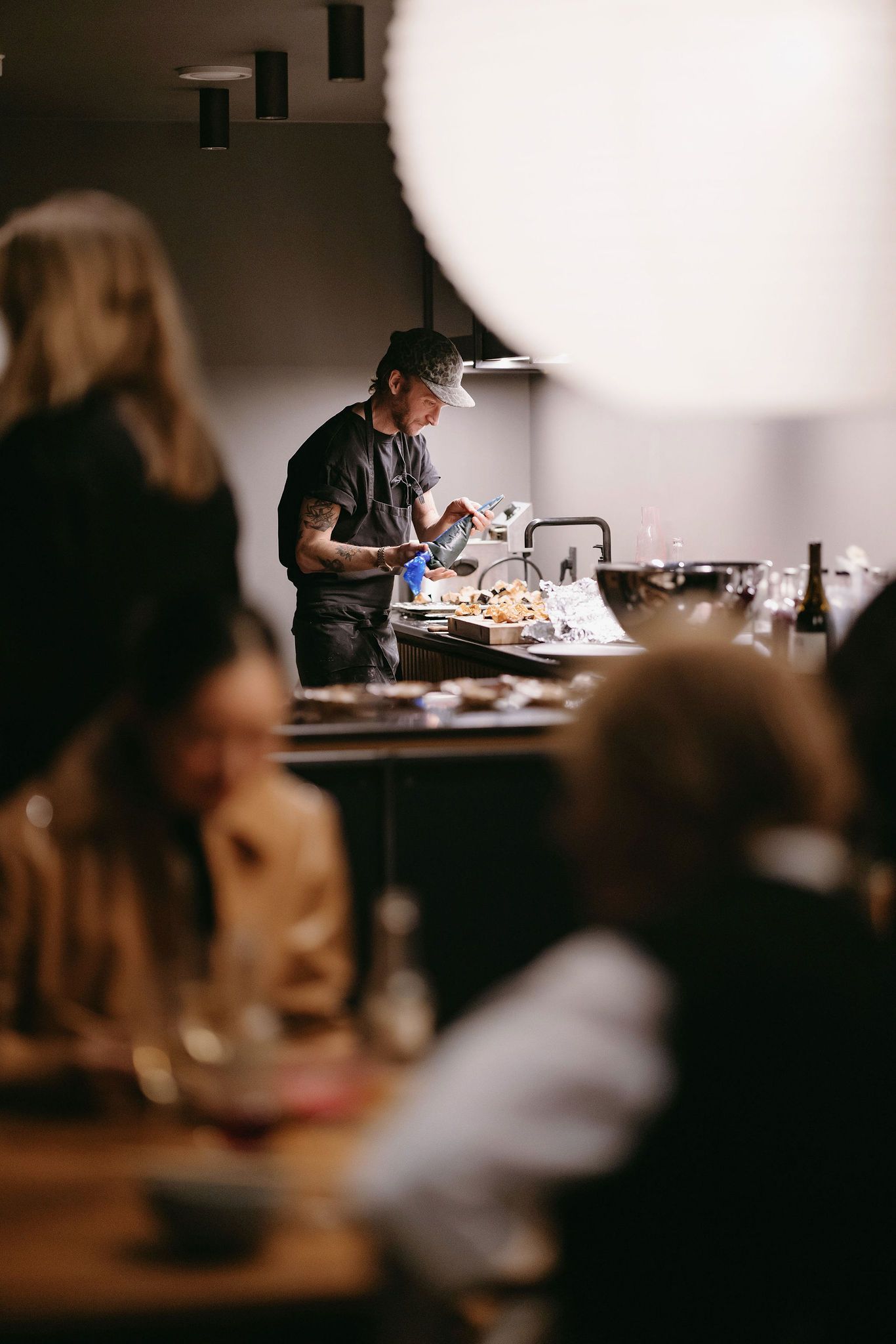 A chef preparing food at a counter while attendees watch from their seats in a dimly lit venue.