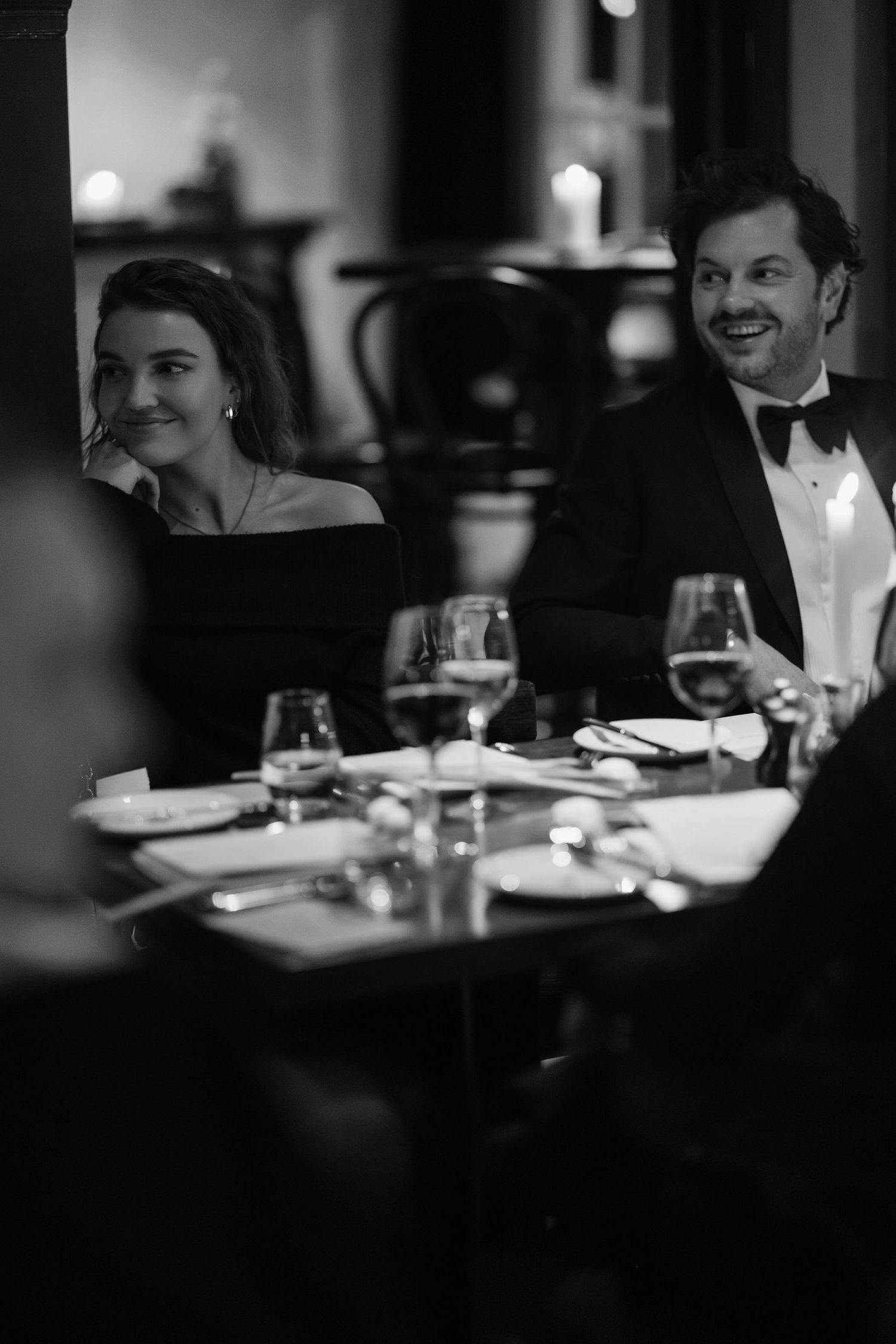 Black and white candid shot of formal dinner guests enjoying conversation at table.