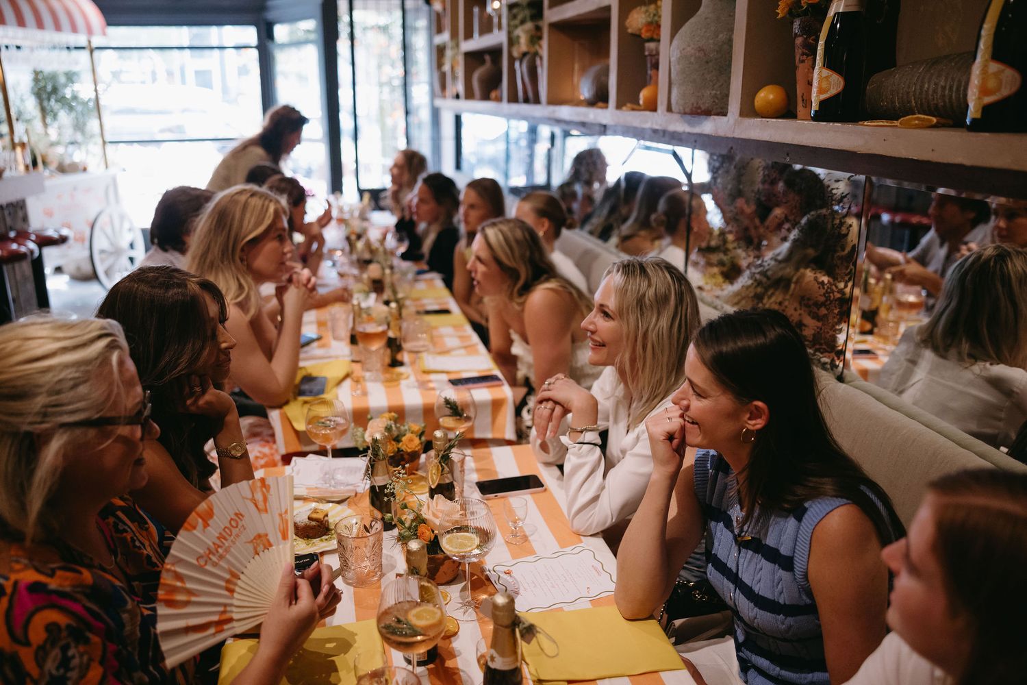 A group dining together at a long table in a restaurant with wine glasses and plates.