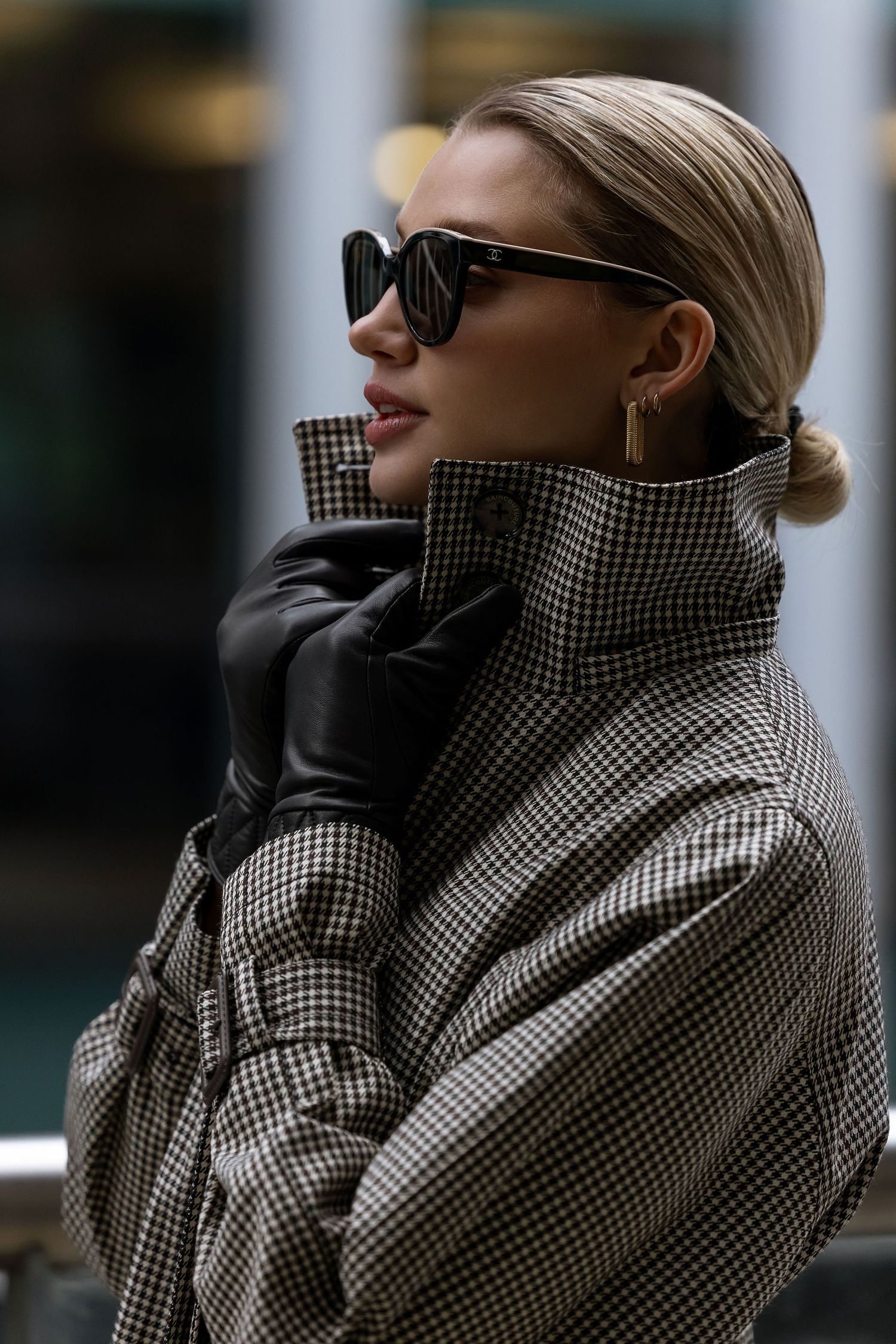 Stylish woman in houndstooth coat and sunglasses with sleek blonde hair.