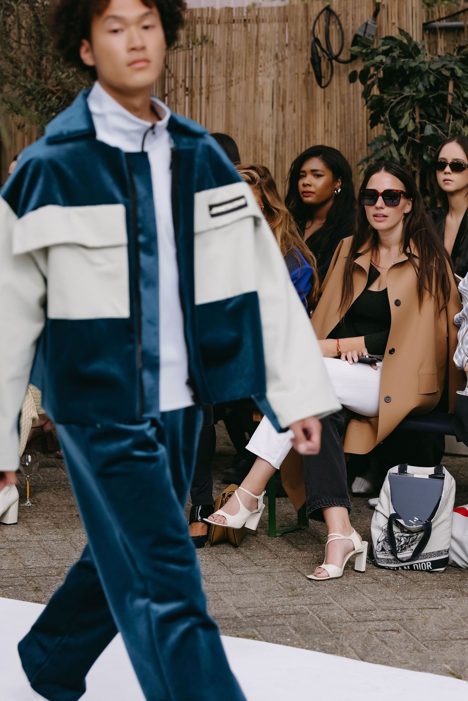 Fashion model walking runway in blue and white outfit as audience watches.