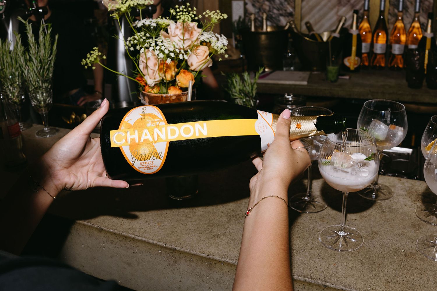 Hands holding a bottle of Chandon champagne at an evening celebration.