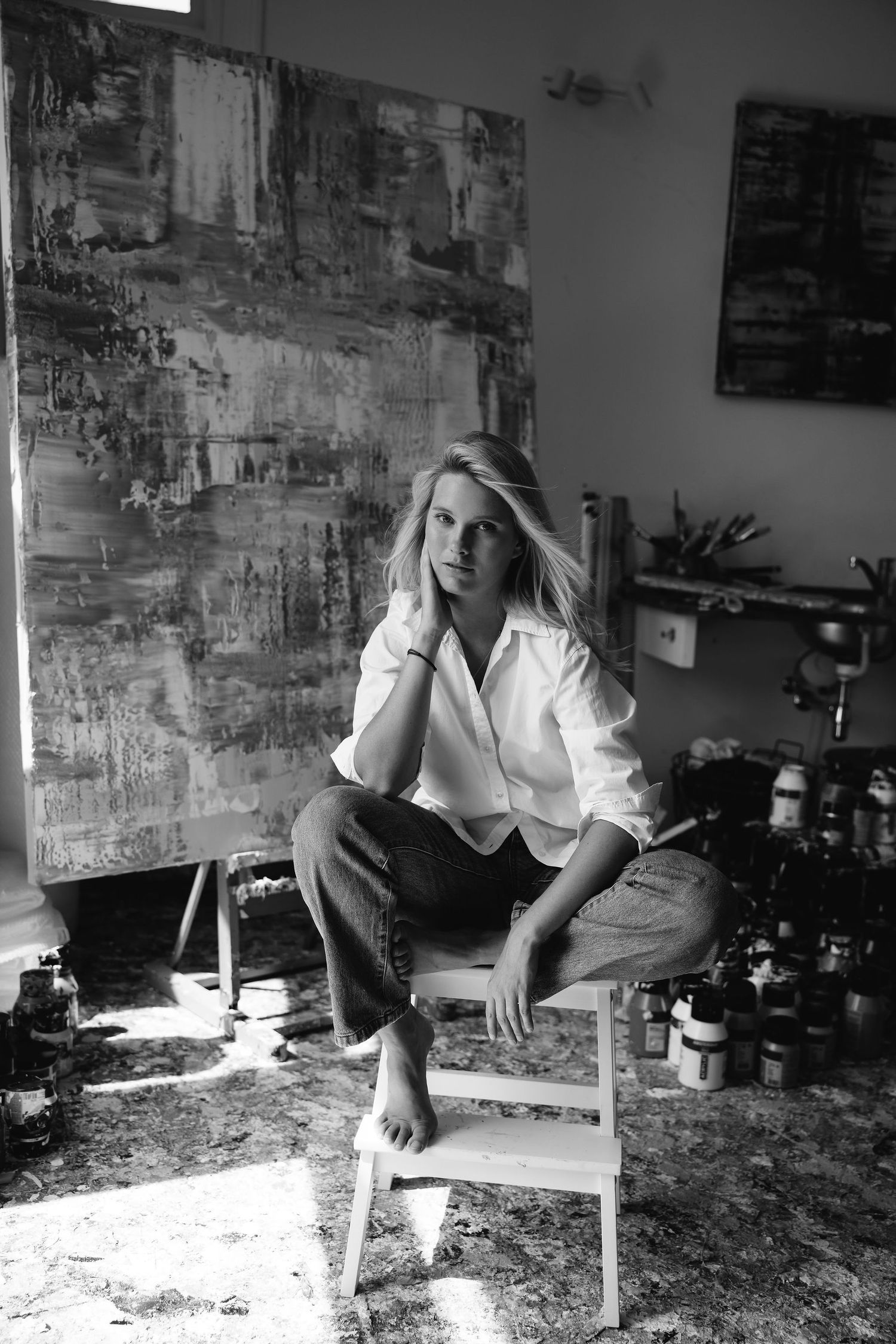Black and white photo of artist sitting in paint-splattered studio with canvas.
