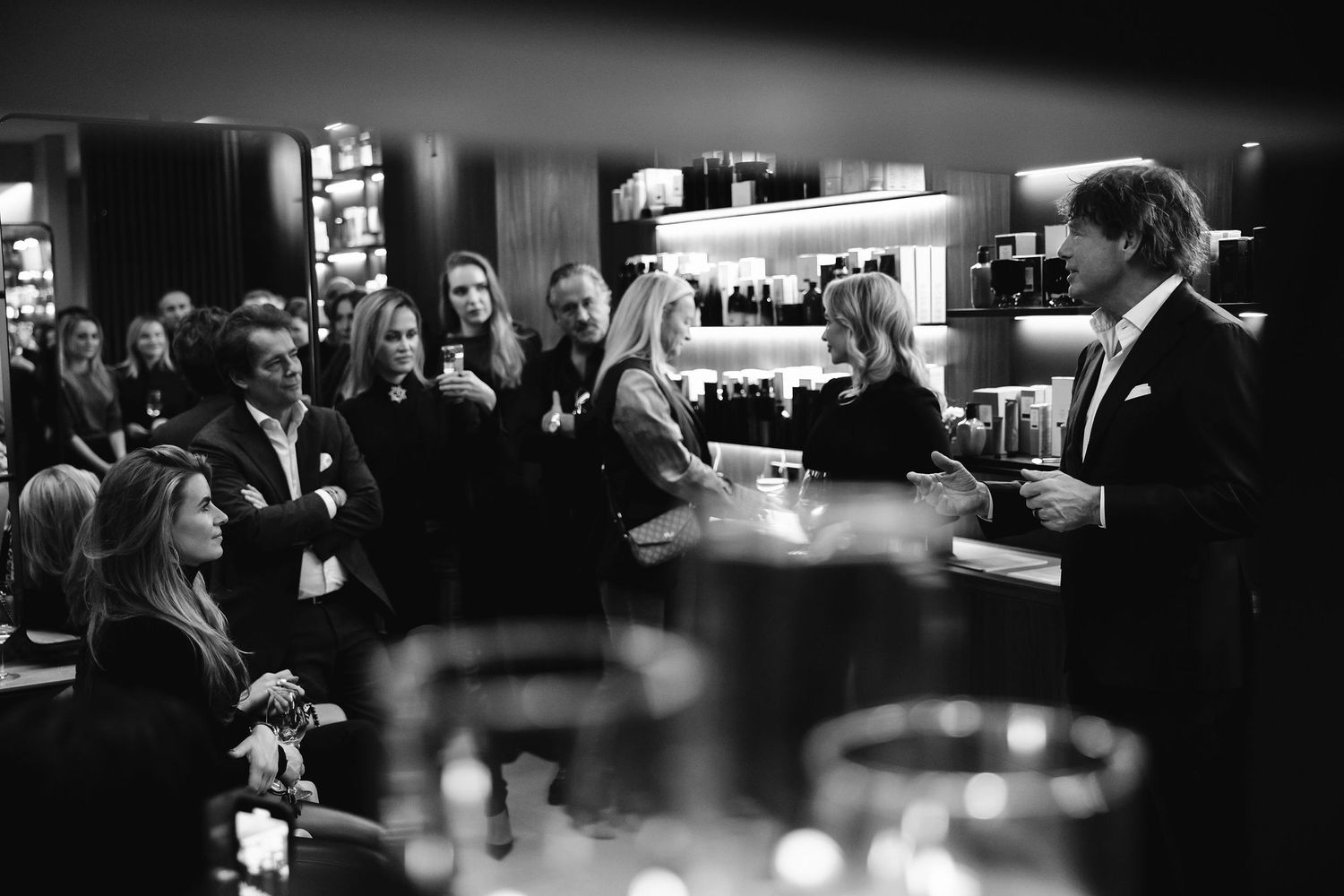 Crowded bar scene in black and white with patrons gathered around a dimly lit counter.