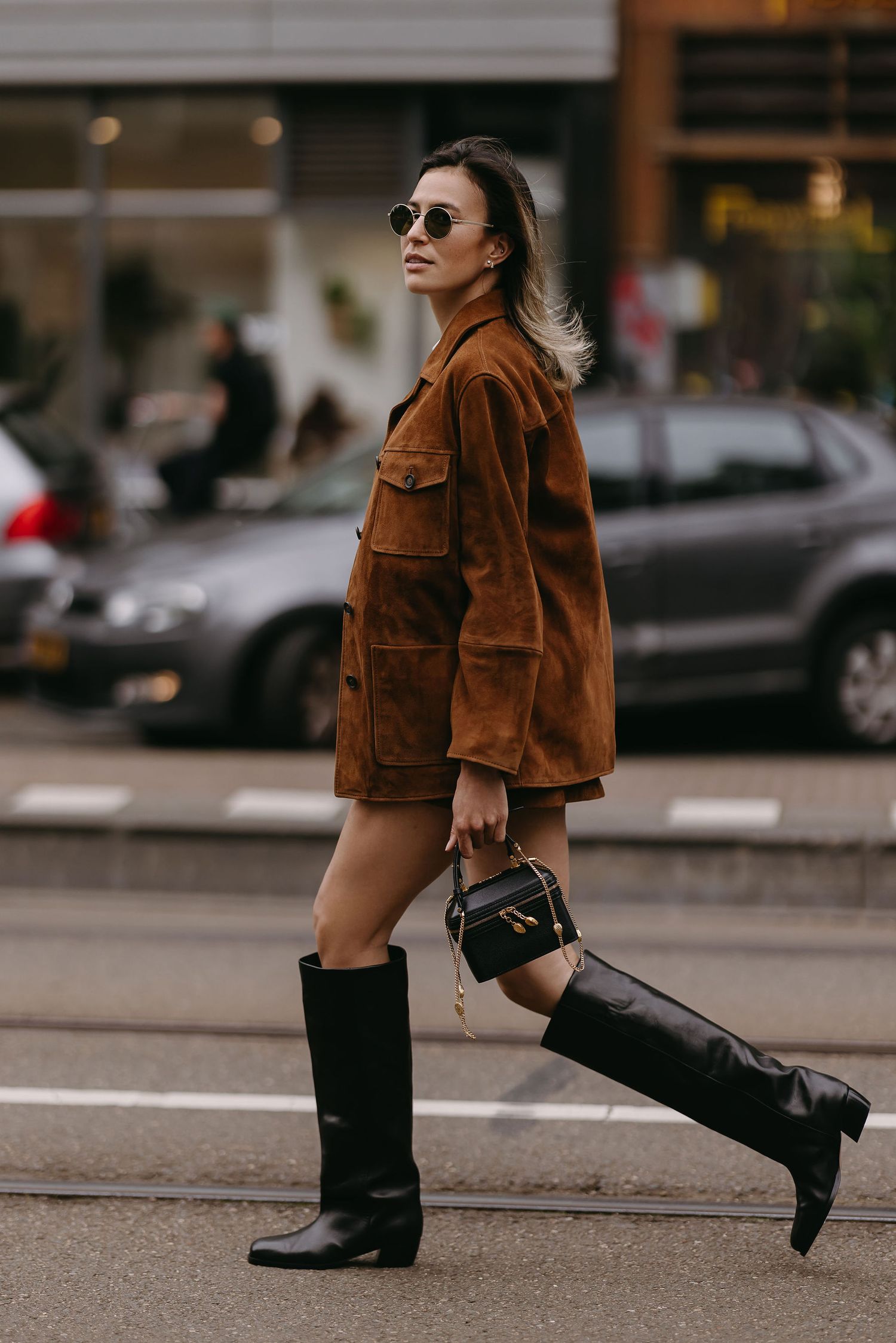 Street style shot of person wearing brown suede jacket and tall black boots.