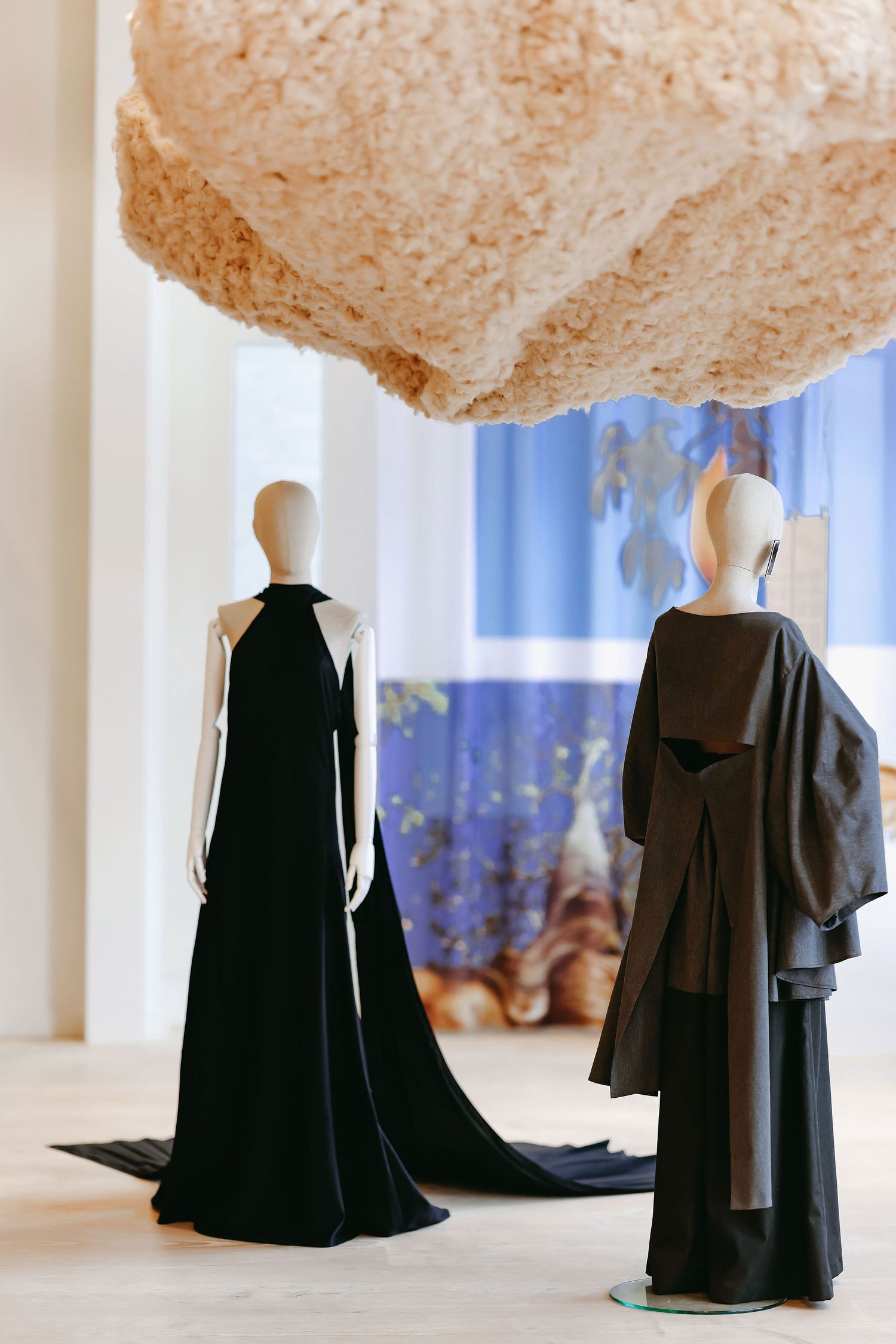 Elegant black evening gowns on mannequins displayed under textured beige ceiling installation.