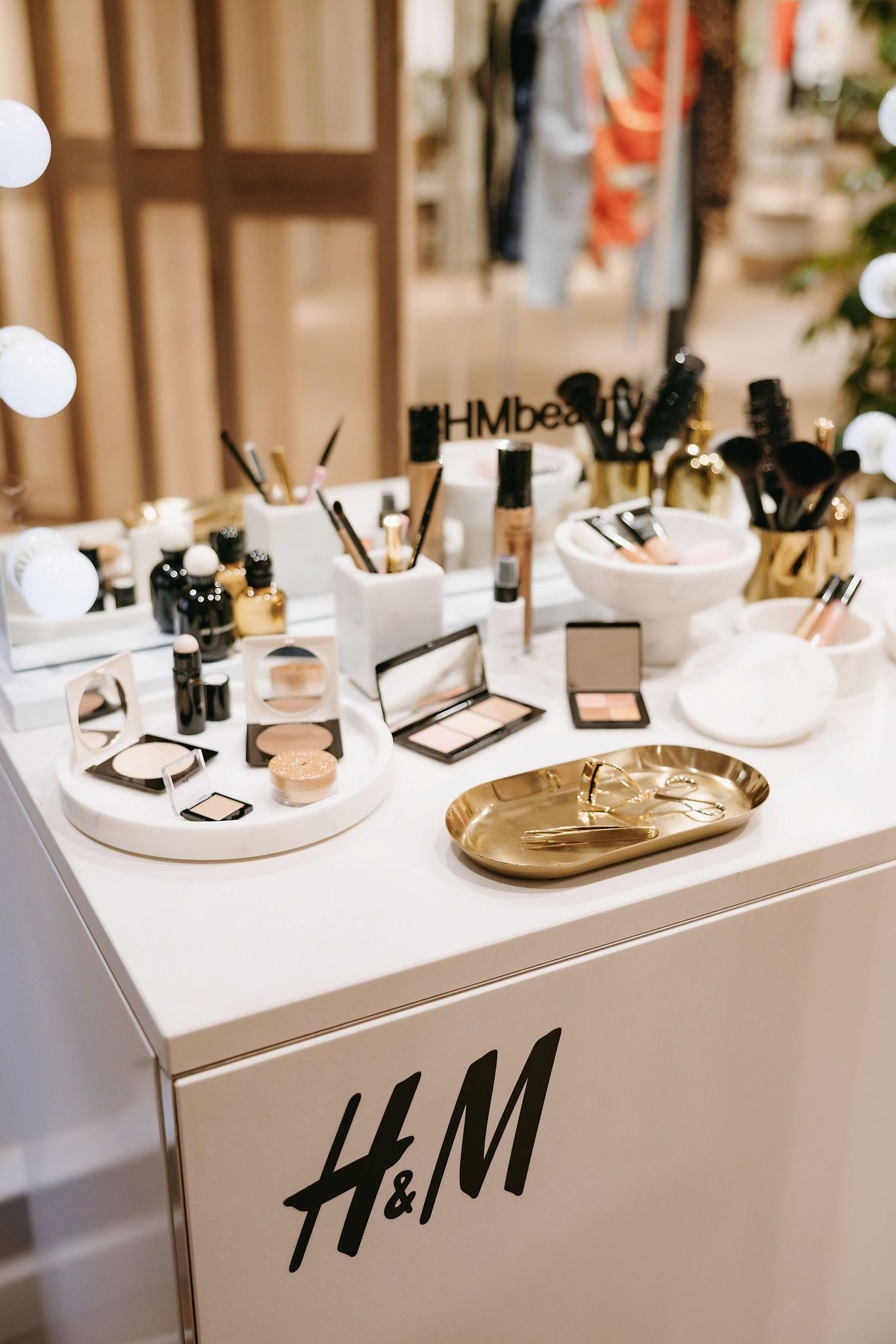 H&M makeup display featuring cosmetics and beauty tools on a white counter.