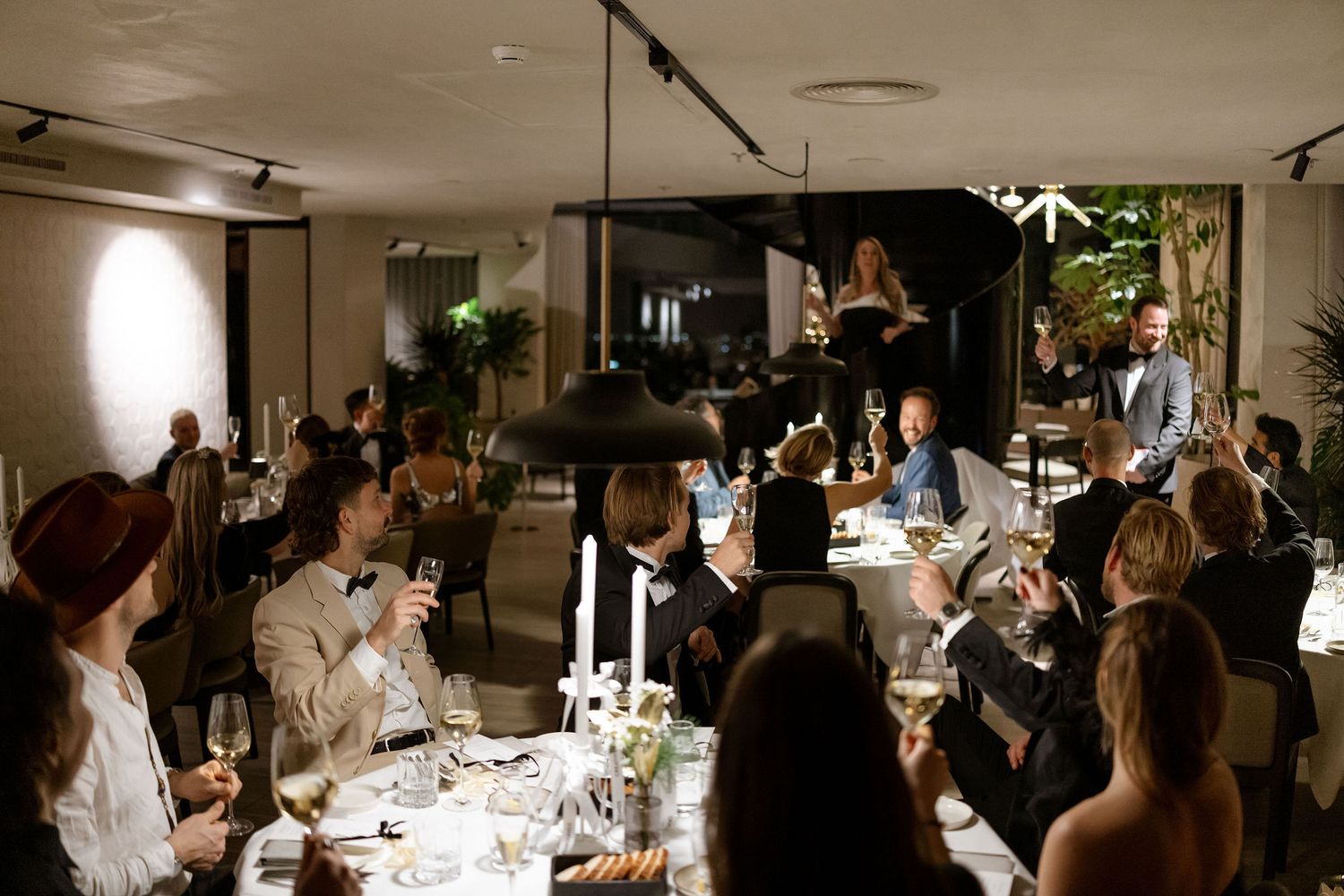 Guests enjoy an intimate candlelit dinner party at a long table in a modern space.