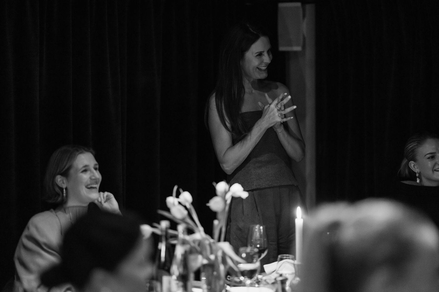 Black and white photo of guests enjoying a lively dinner party with candlelit ambiance.