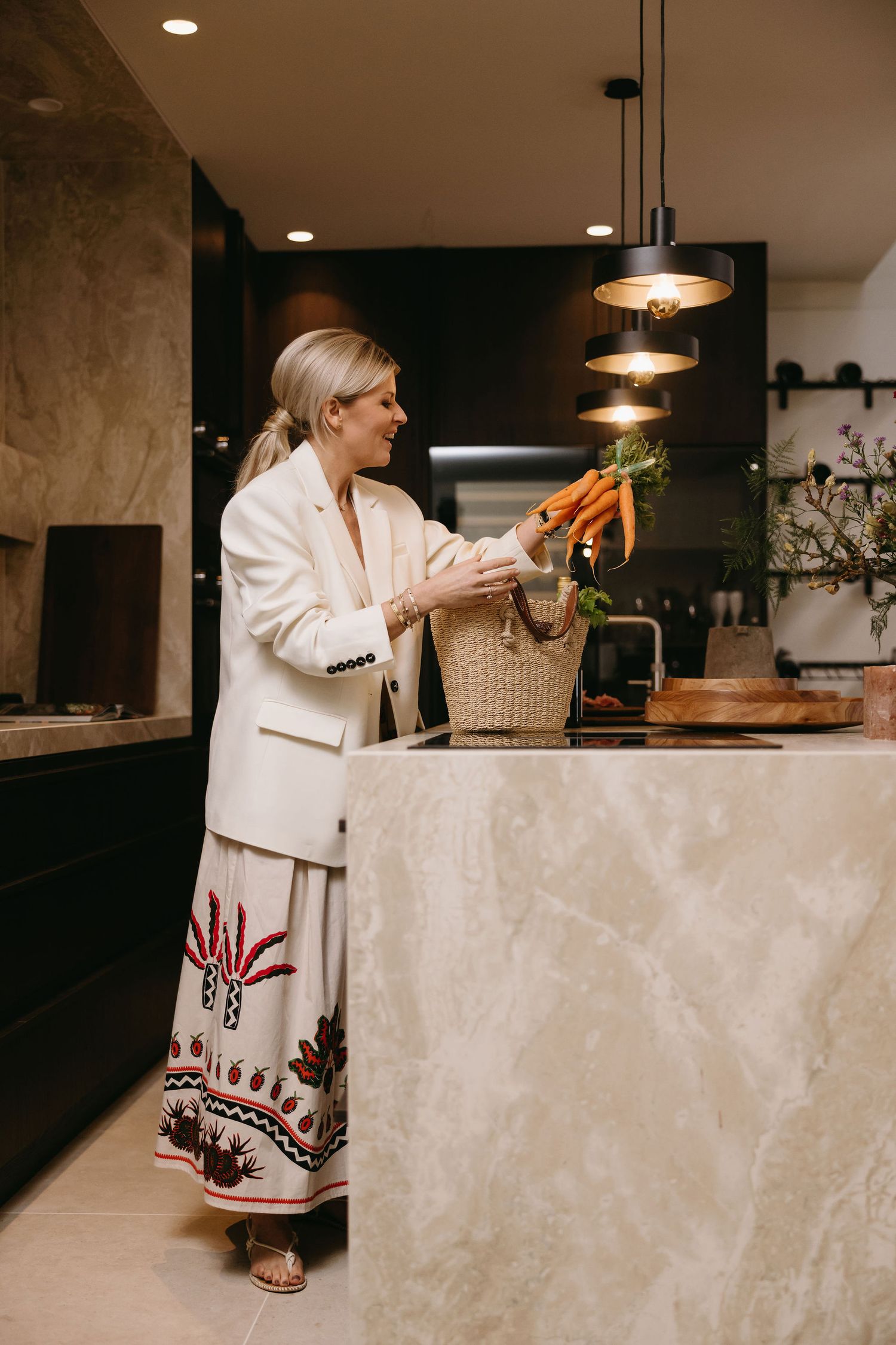 Person in white blazer and patterned maxi skirt sorting through vegetables at a kitchen counter.