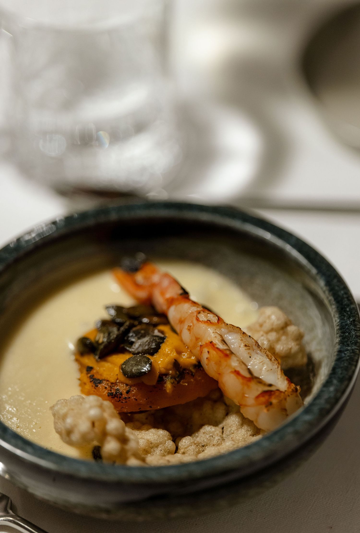 Gourmet seafood dish with shrimp and garnishes served in a rustic ceramic bowl with cream sauce.