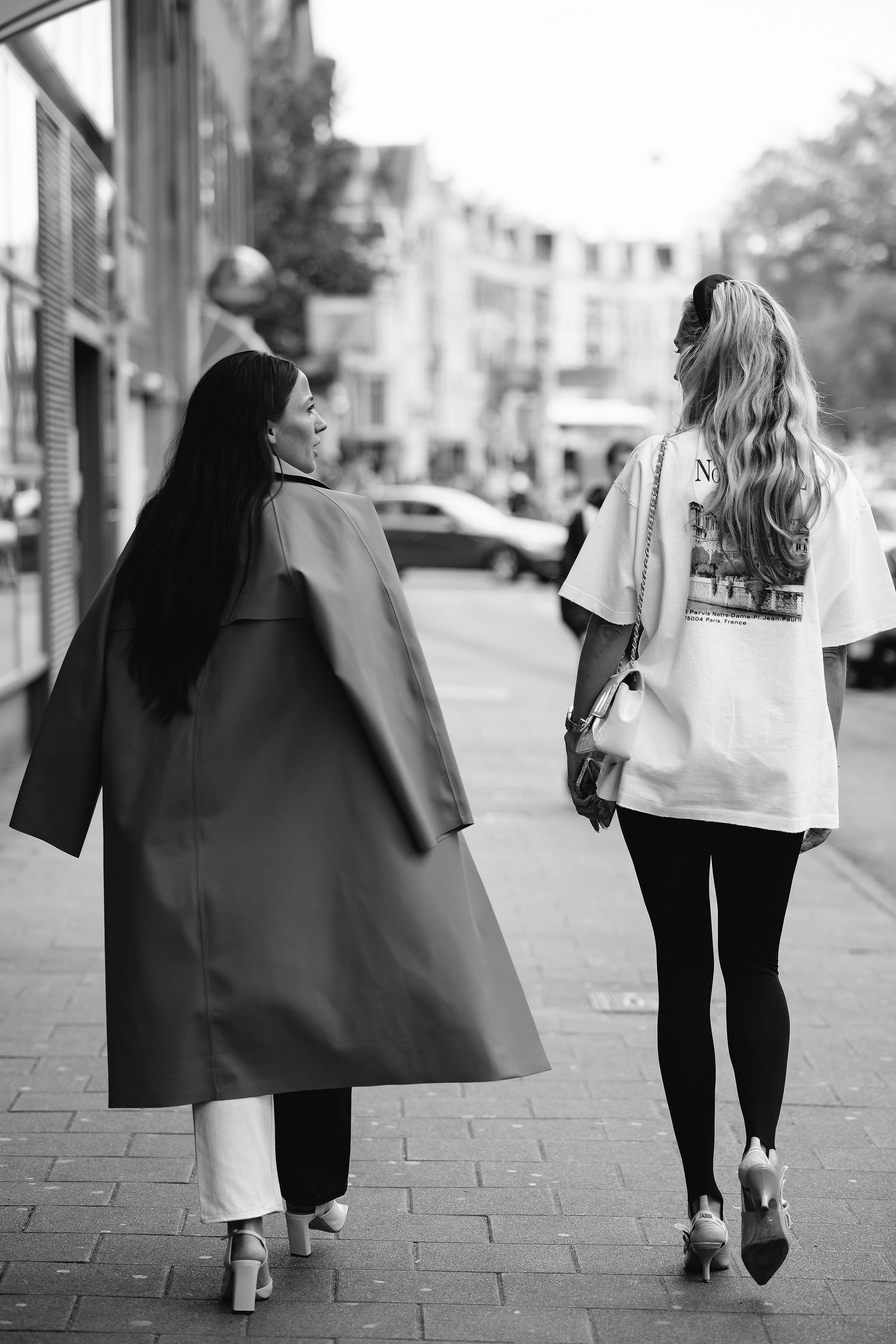 Two stylish women walking down urban sidewalk in black and white photography.