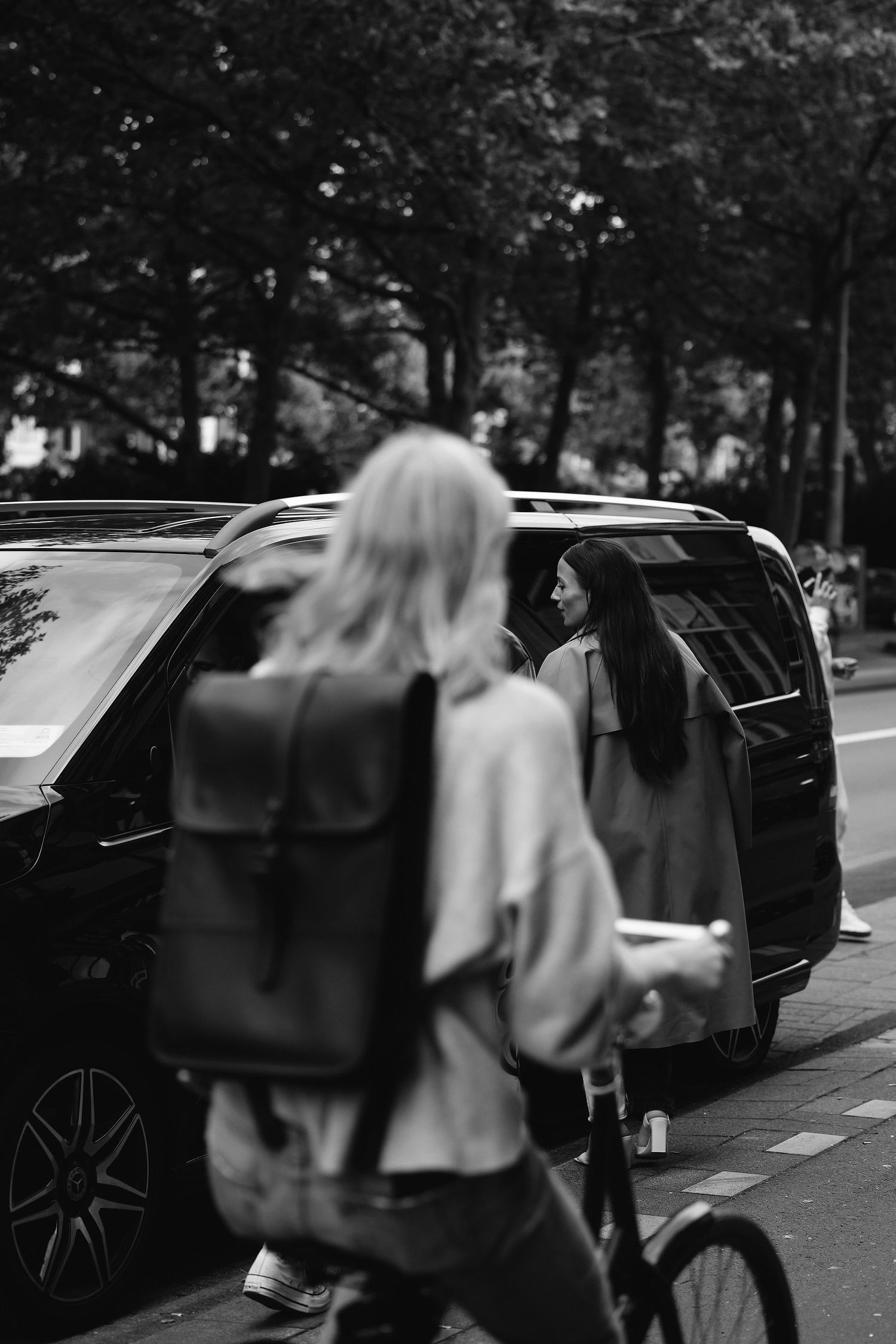 Black and white street scene with person entering luxury vehicle.