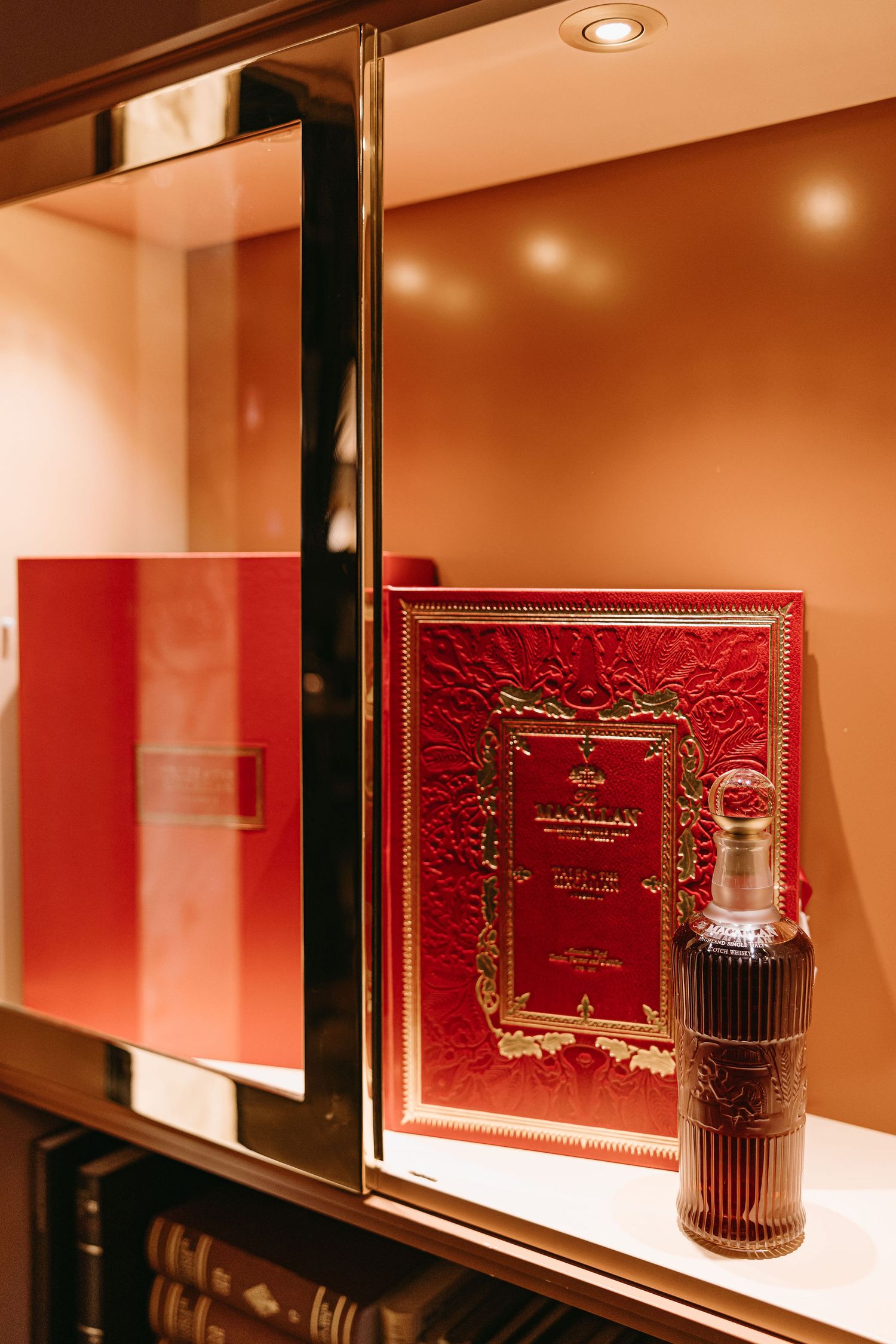 Elegant red leather-bound book and decorative bottle displayed on illuminated shelf.