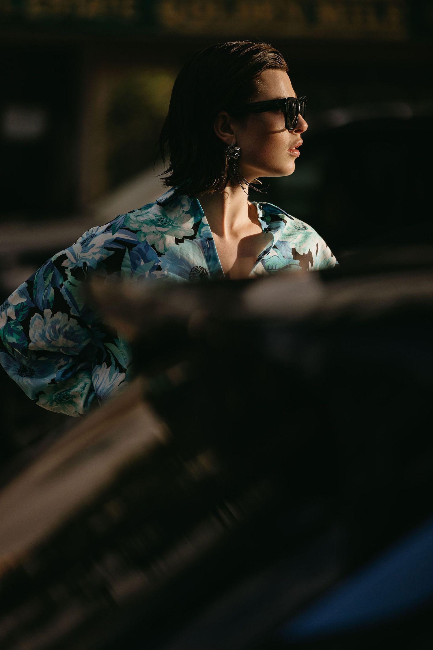 Fashion portrait of a model wearing a floral Hawaiian shirt and sunglasses in dramatic lighting.