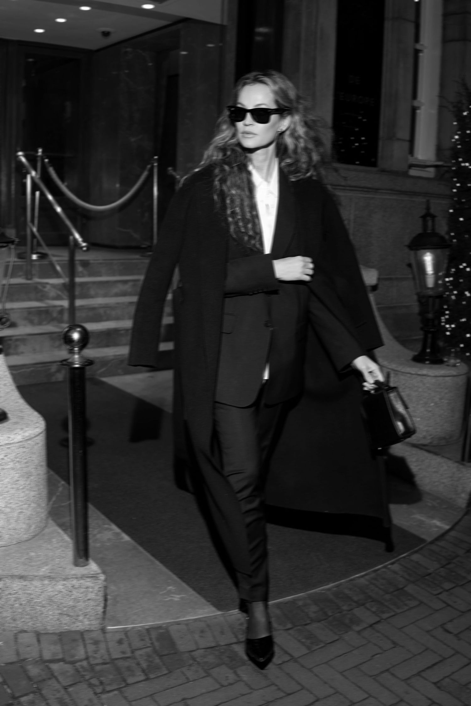 Classic black and white fashion photo on steps with long coat and heels.