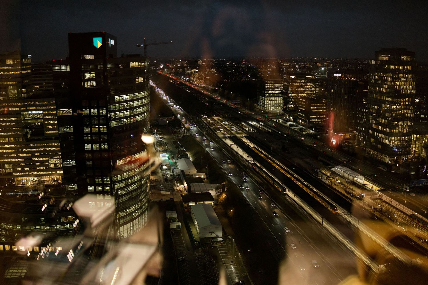 Night cityscape showing illuminated buildings and light trails from traffic on busy streets.