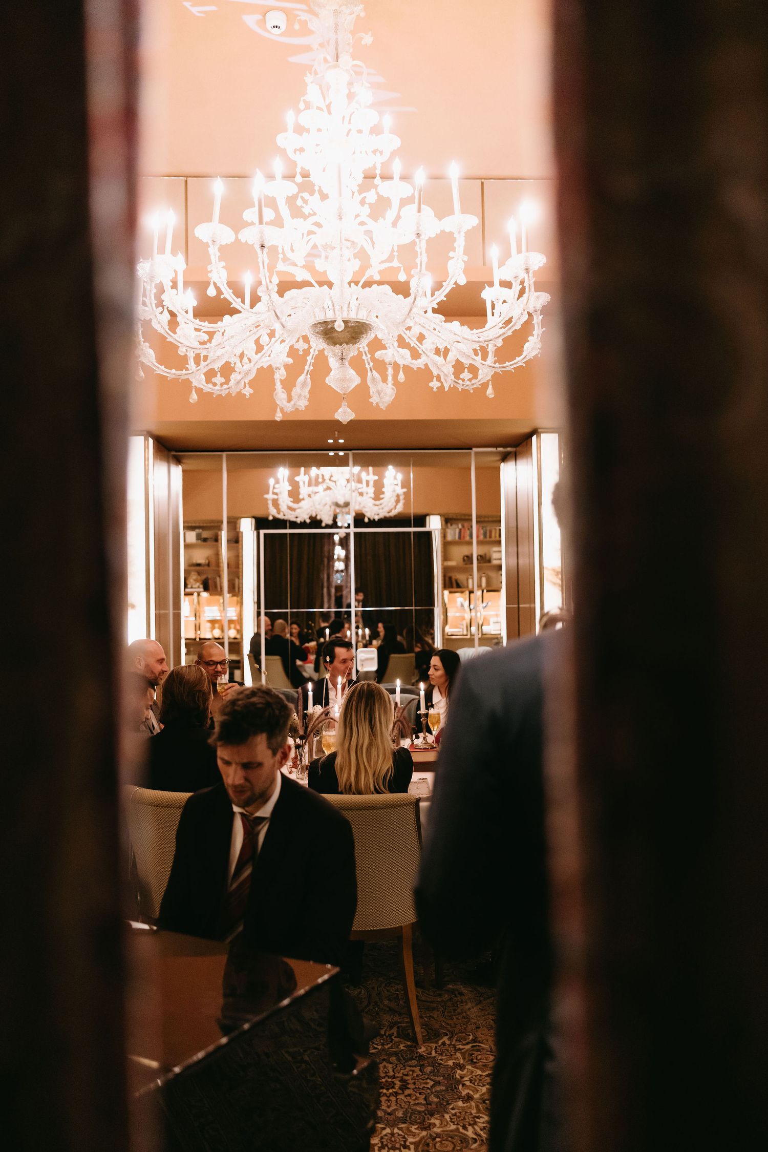 Elegant dining room with crystal chandelier and guests seated at tables in warm ambient lighting.
