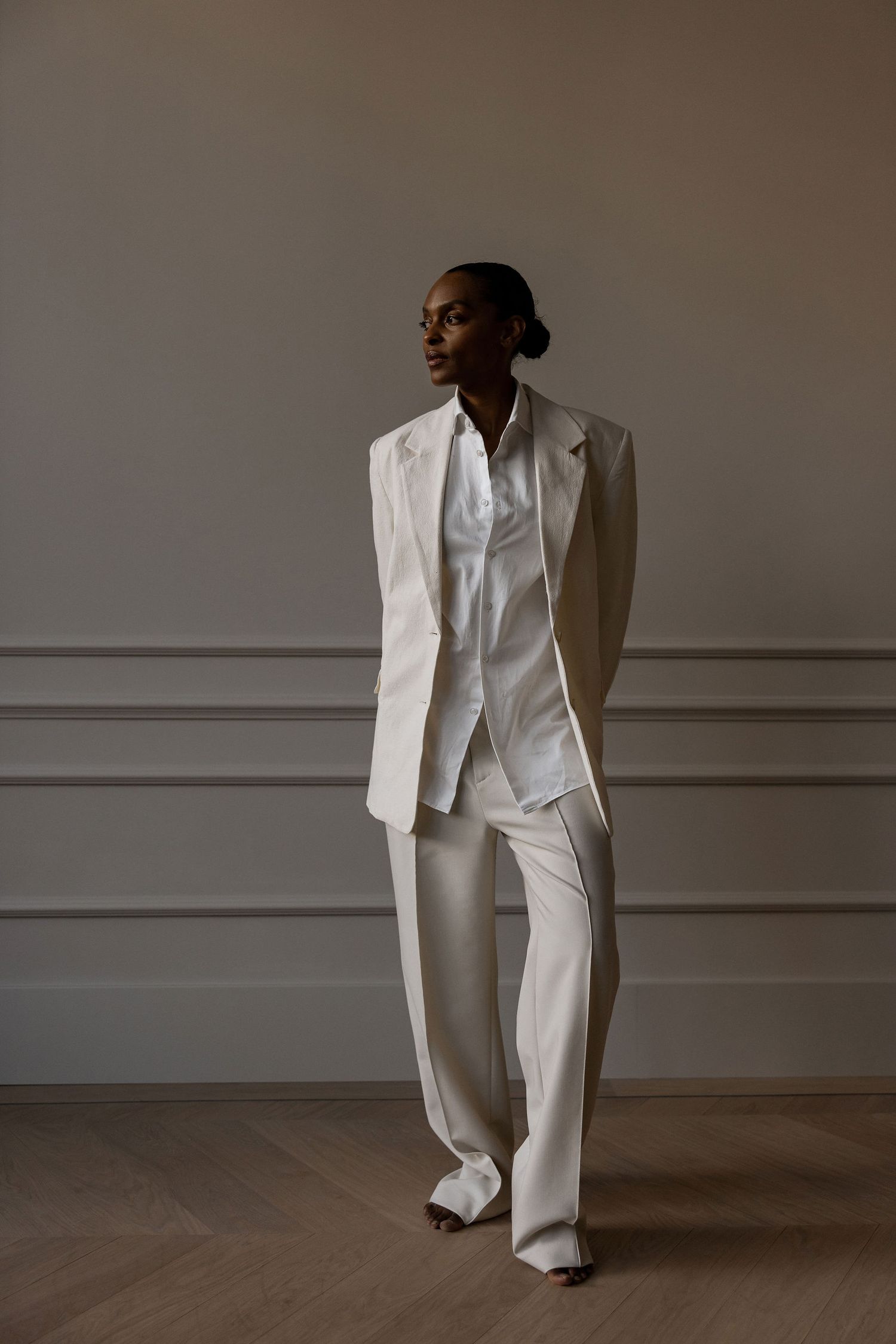 Fashion model in an oversized white power suit with luxurious draping against a neutral wall.