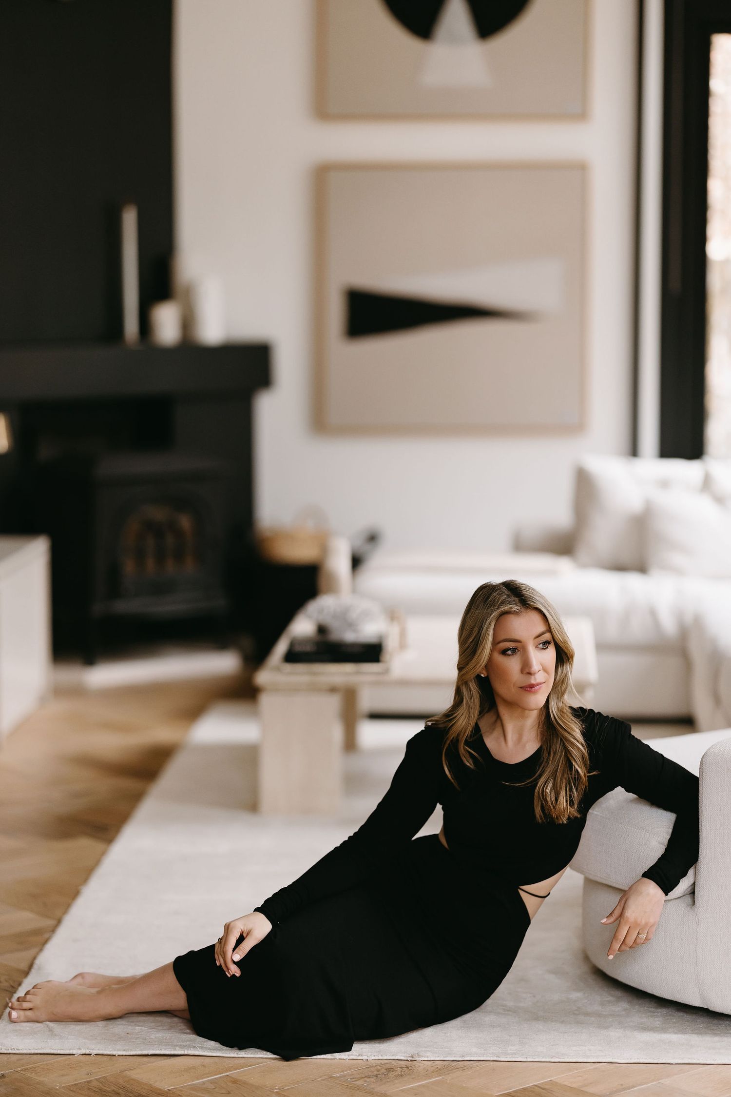 Elegant portrait in black dress lounging on light carpet near fireplace.