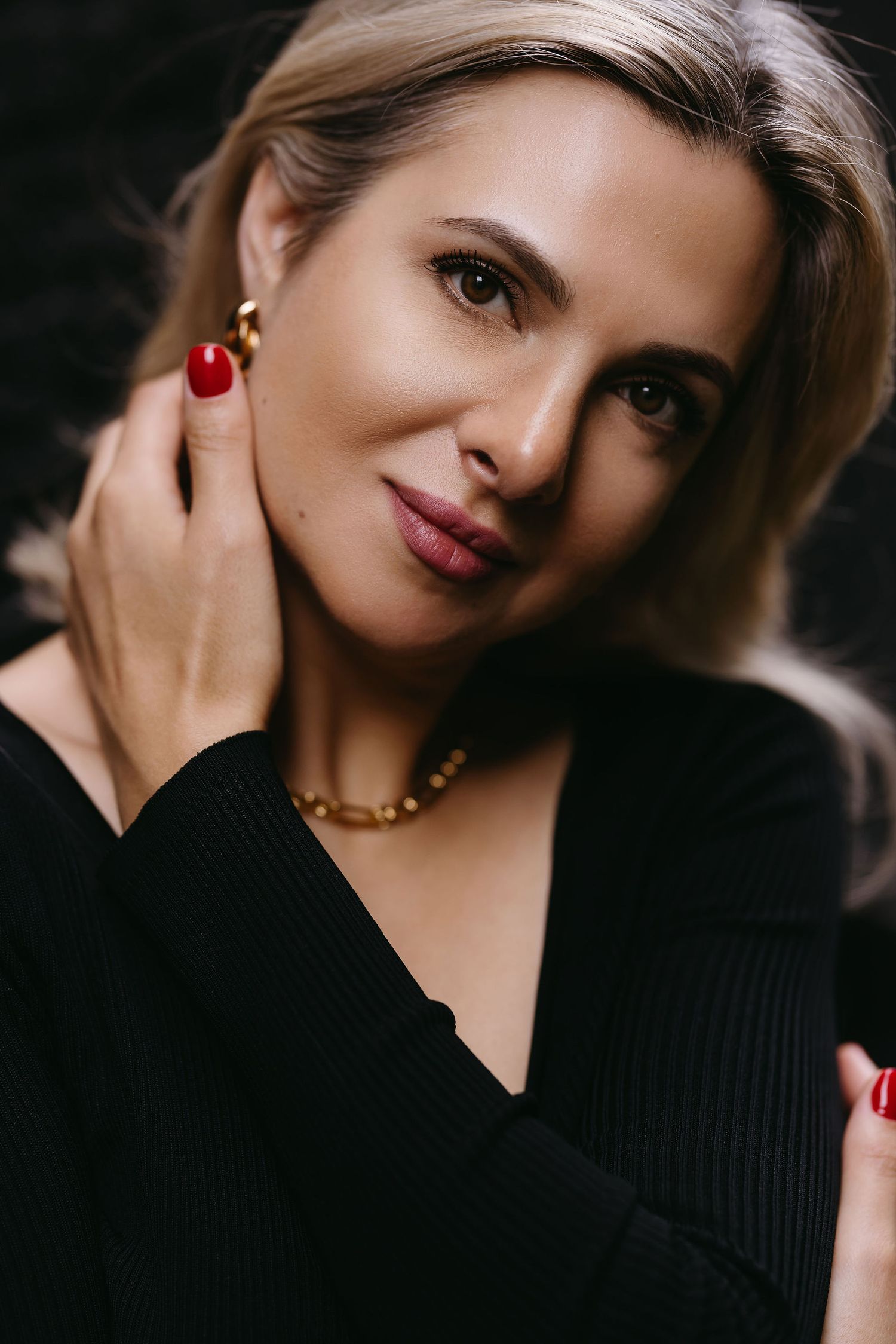 Close-up portrait in black sweater with red nails and gold necklace.