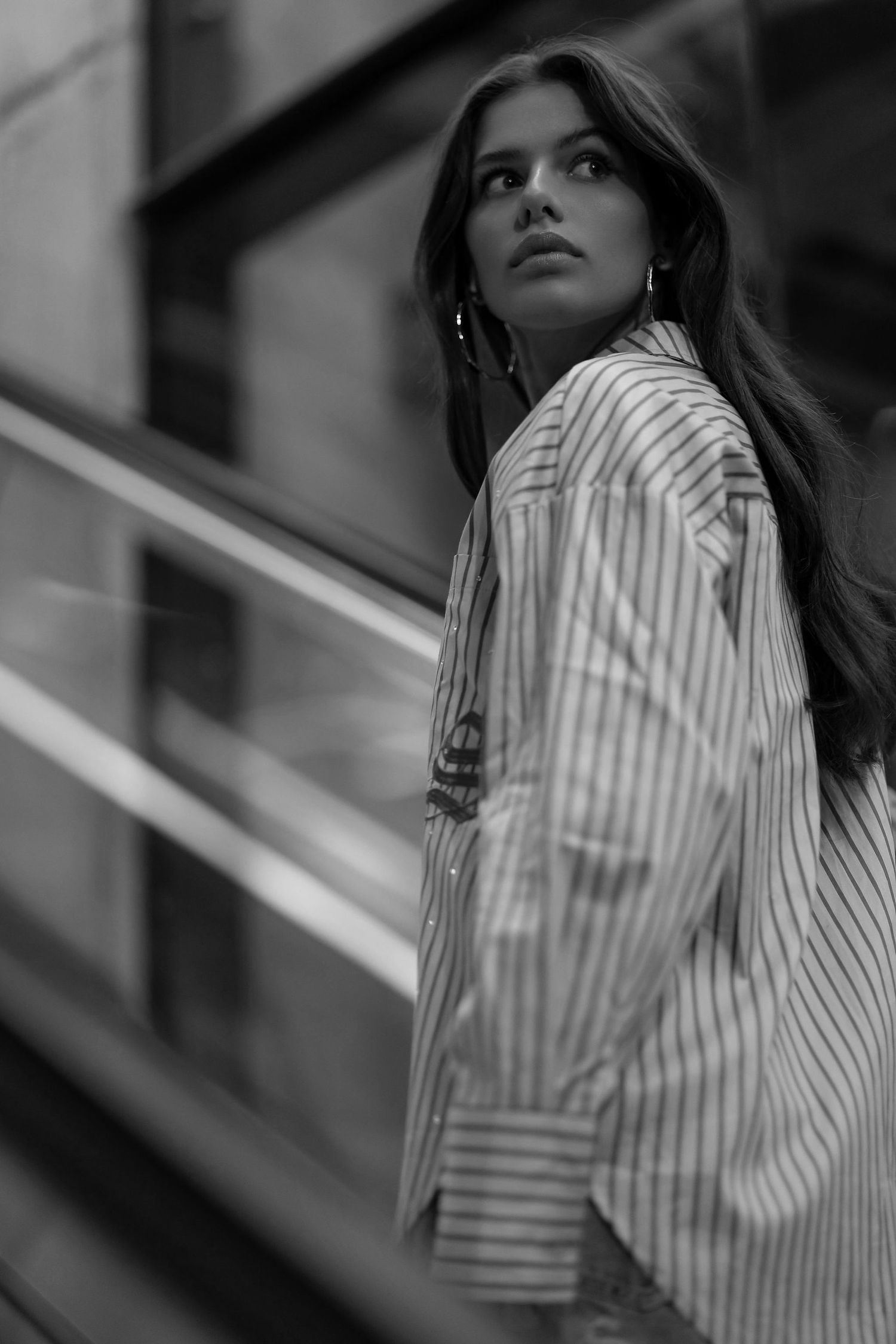 Black and white portrait of model in striped shirt looking over shoulder on staircase.