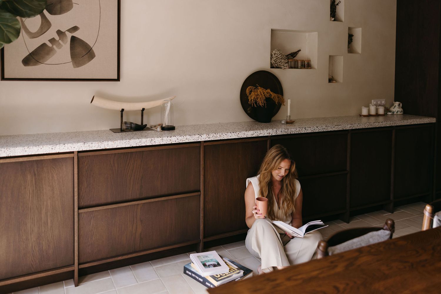 Person relaxing on floor beside modern wooden cabinet with minimalist decor and white walls.